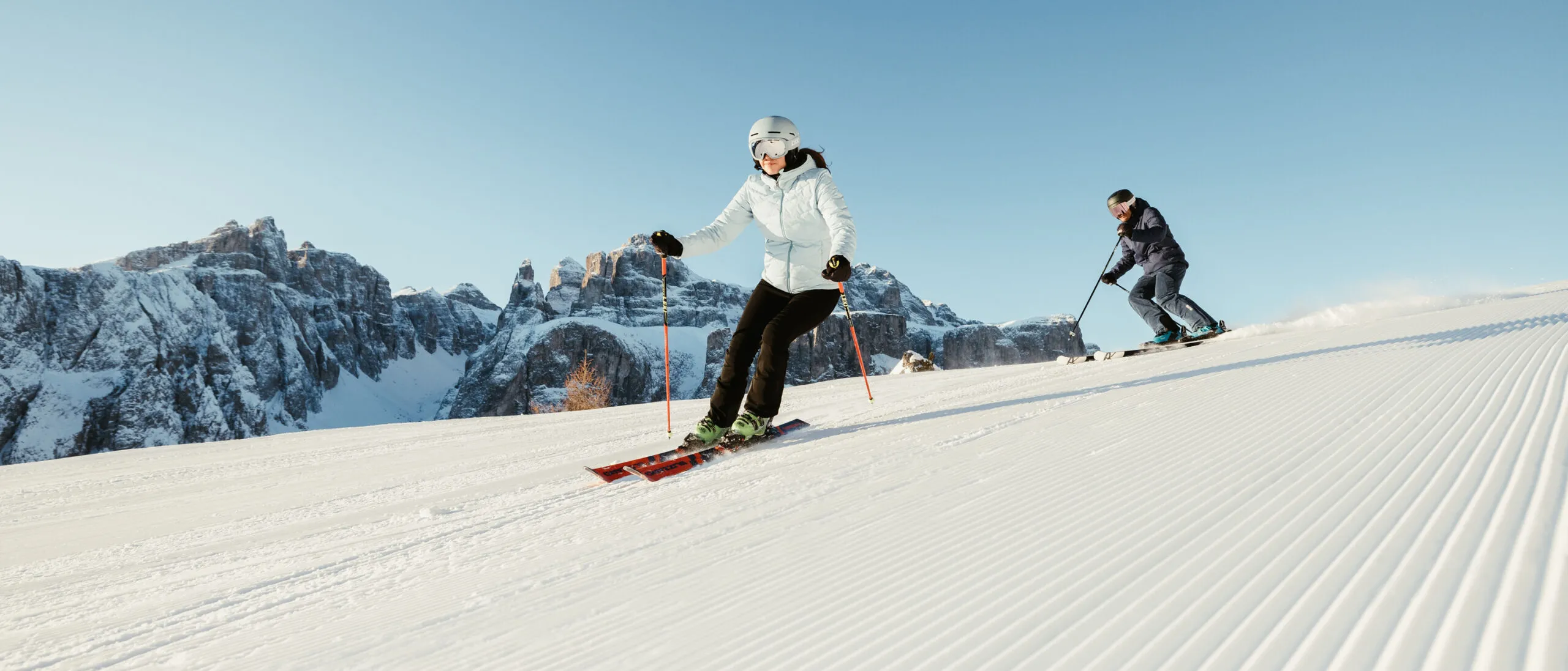 Skier in white jacket and helmet skiing on groomed slope with snow-capped mountains in background