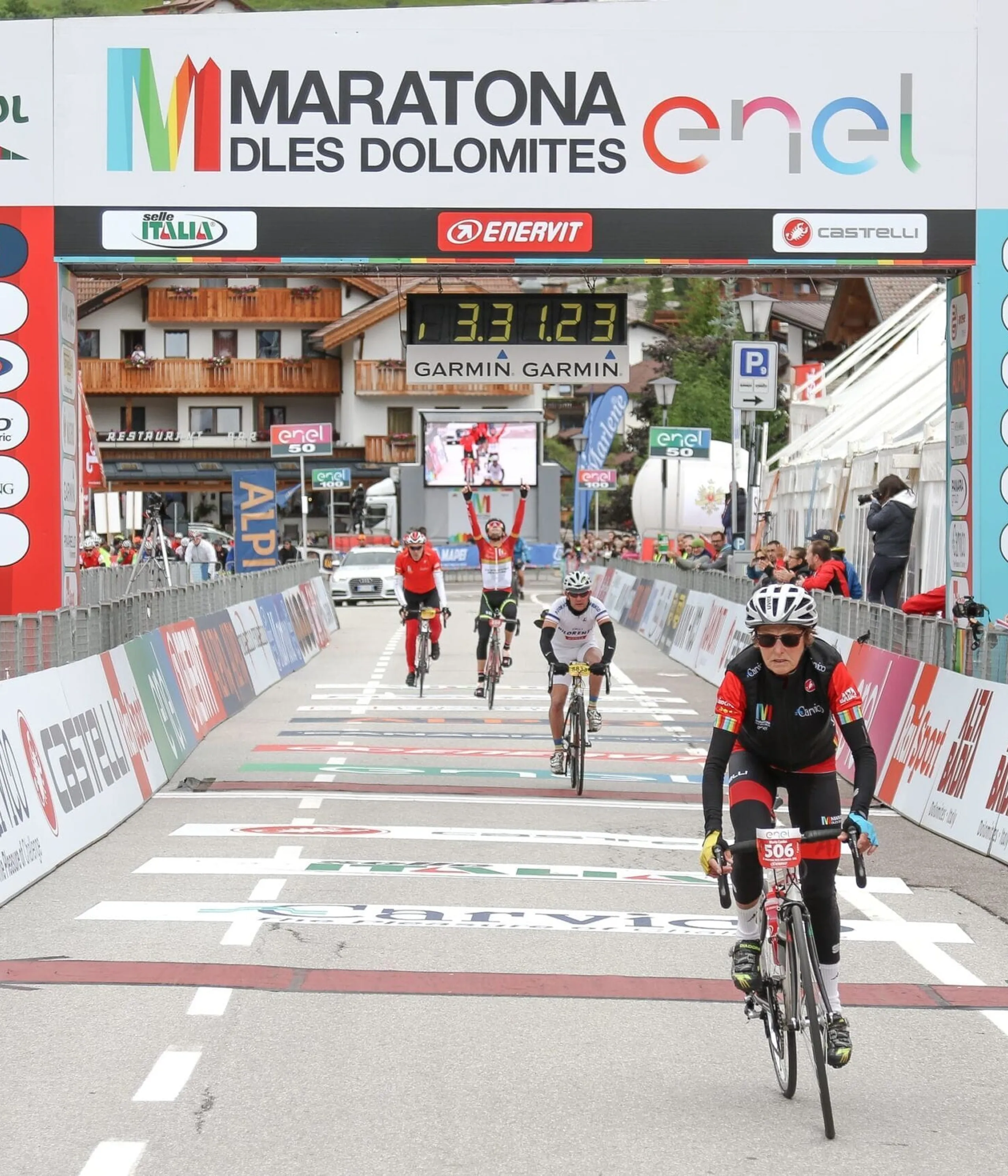 Cyclist crossing finish line at Maratona dles Dolomites with banners and cheering crowd in Alta Badia.