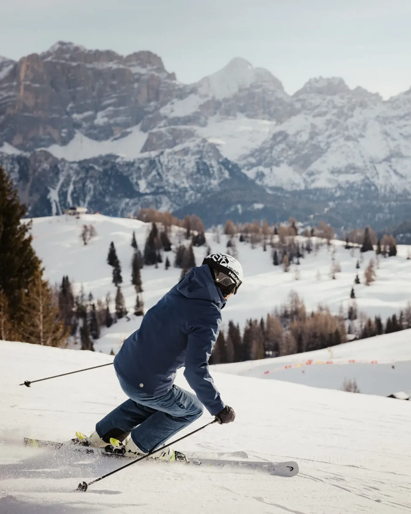 Skier in blue jacket and helmet carving down a snowy slope with mountains in the distance.