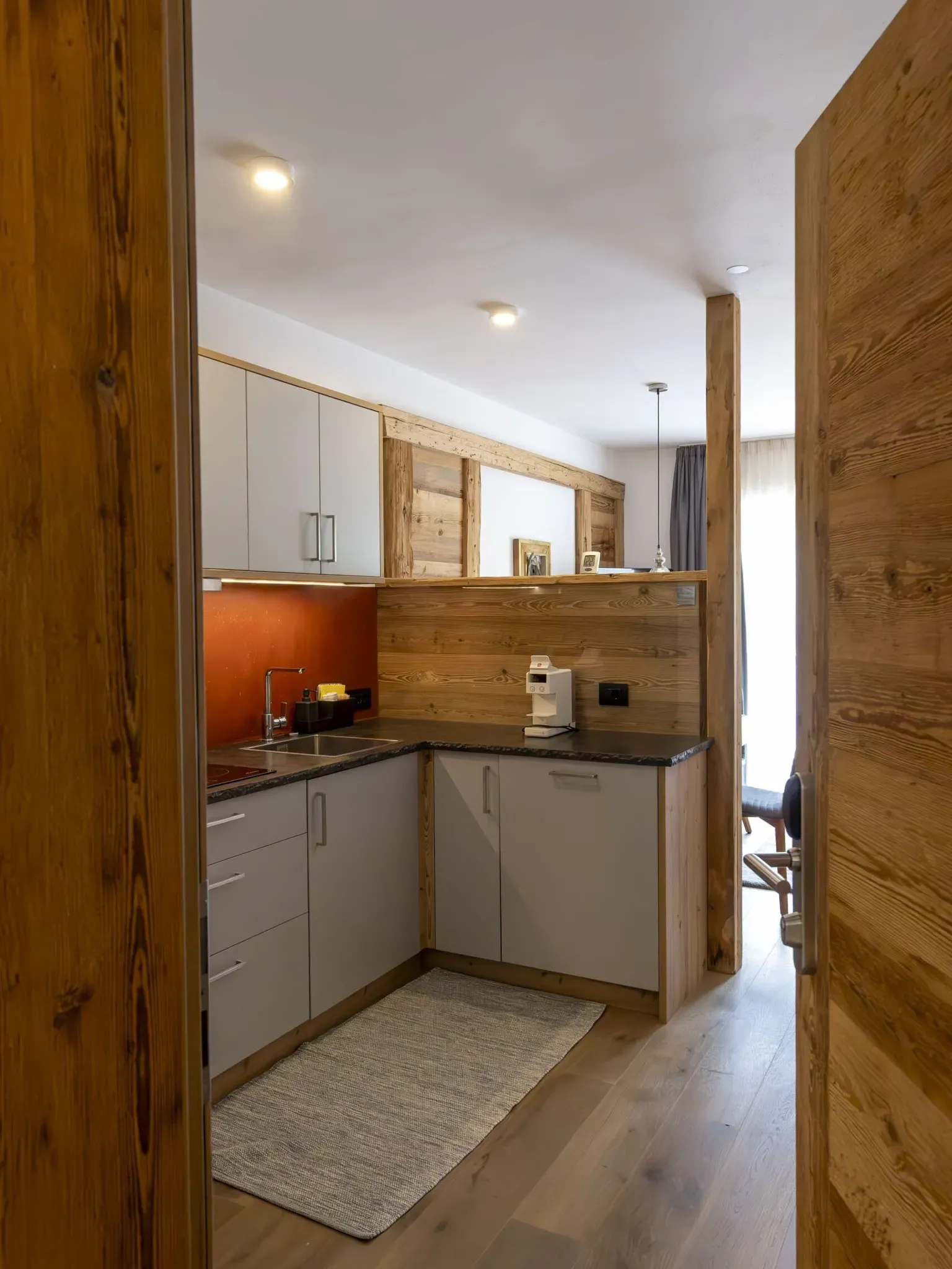 Compact modern kitchen with light gray cabinets, wooden accents, red backsplash, and small appliances.