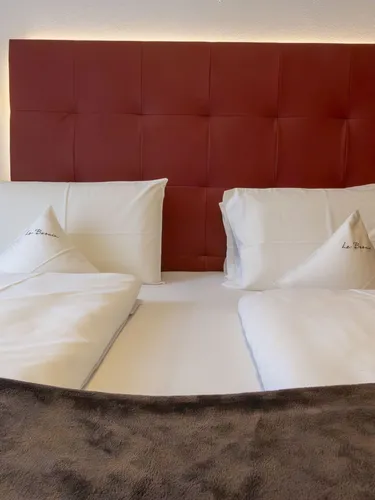 Two white-pillowed beds with a red tufted headboard in a modern hotel room, side lamps, and wooden accents.