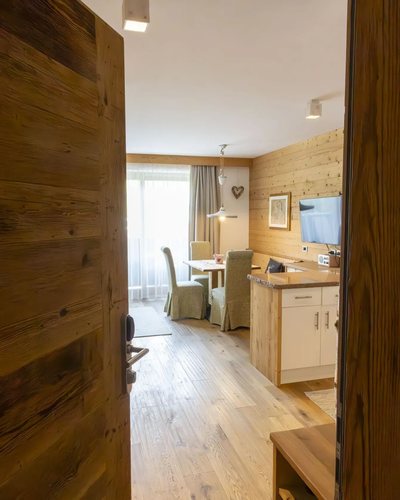 Cozy wooden interior of a dining living area with a dining table, upholstered chairs, and a TV on a wood-paneled wall.