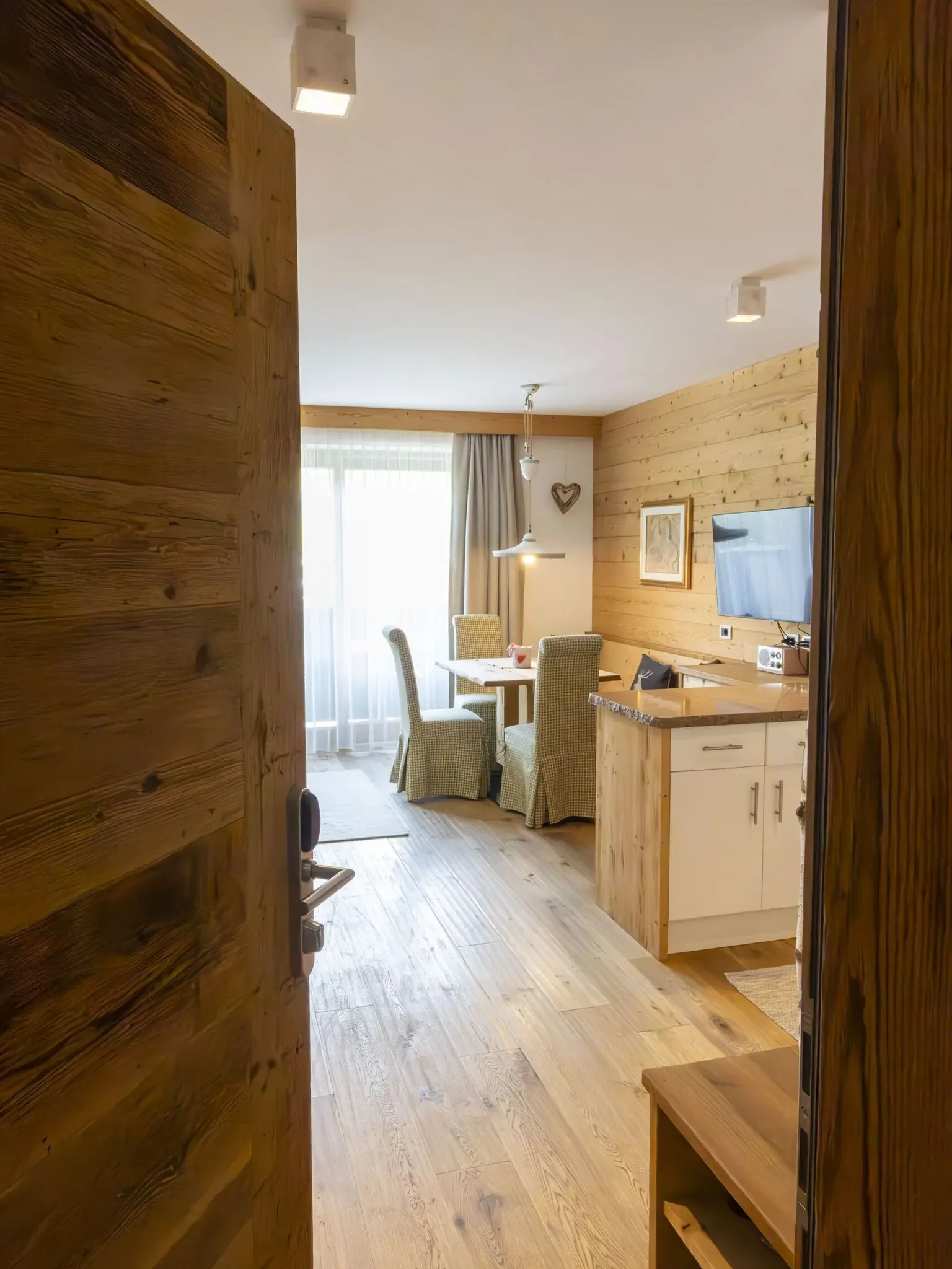 Cozy wooden interior of a dining living area with a dining table, upholstered chairs, and a TV on a wood-paneled wall.