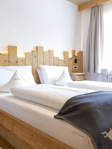 Twin wooden bed with white linens and a dark grey throw, rustic headboard, bedside cabinets, and soft natural light.