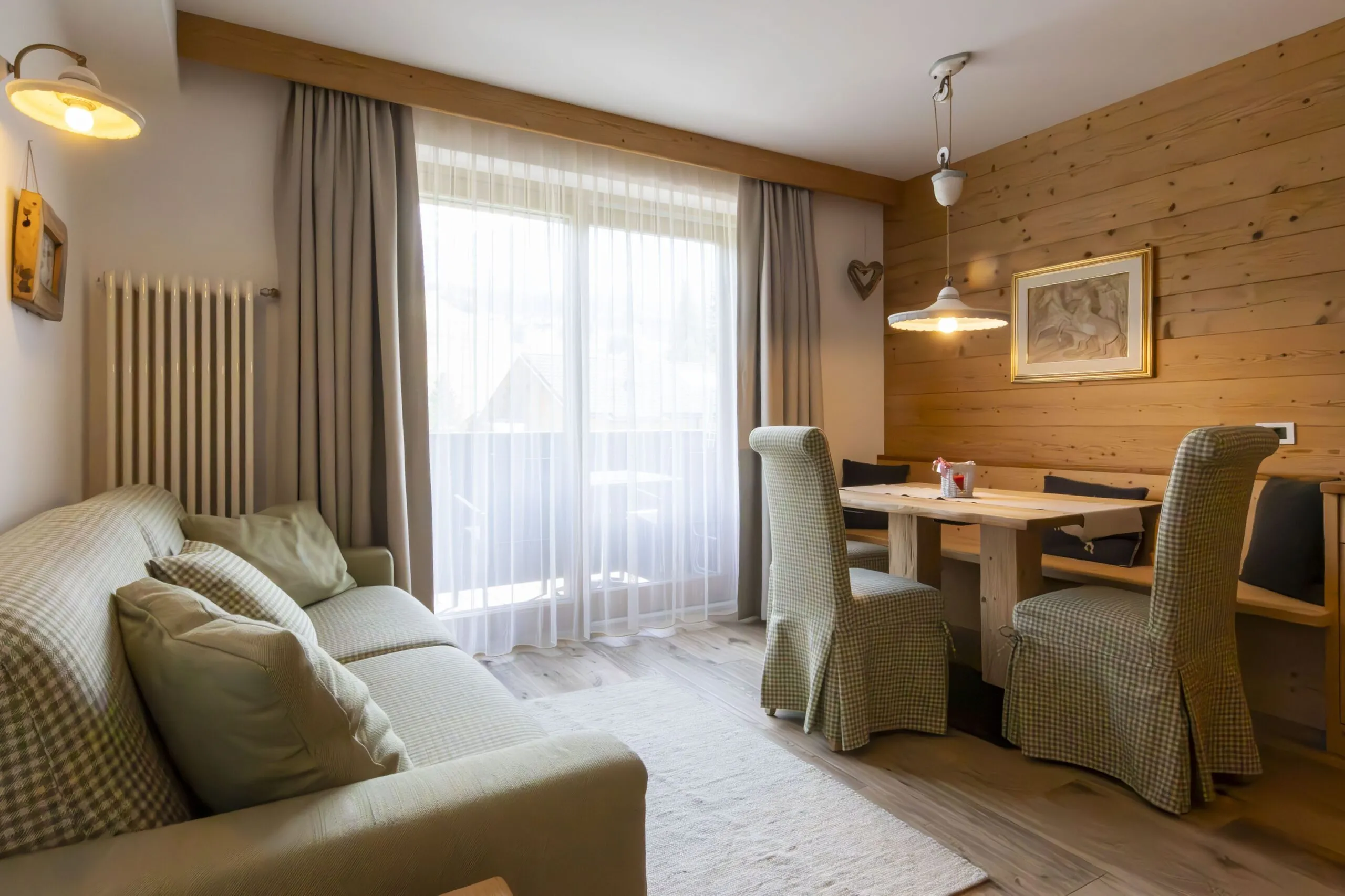 cozy living area with plaid sofa, wooden walls, dining table with cushioned chairs, large window with sheer curtains