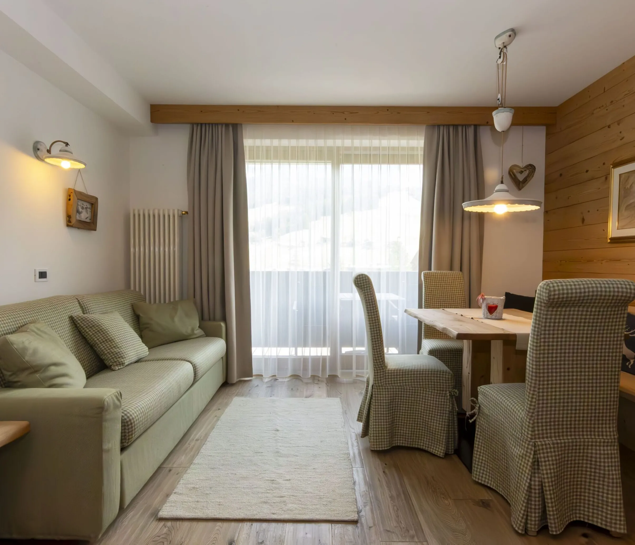 Cozy living and dining area with plaid sofa, wooden walls, and a dining table by a large window.