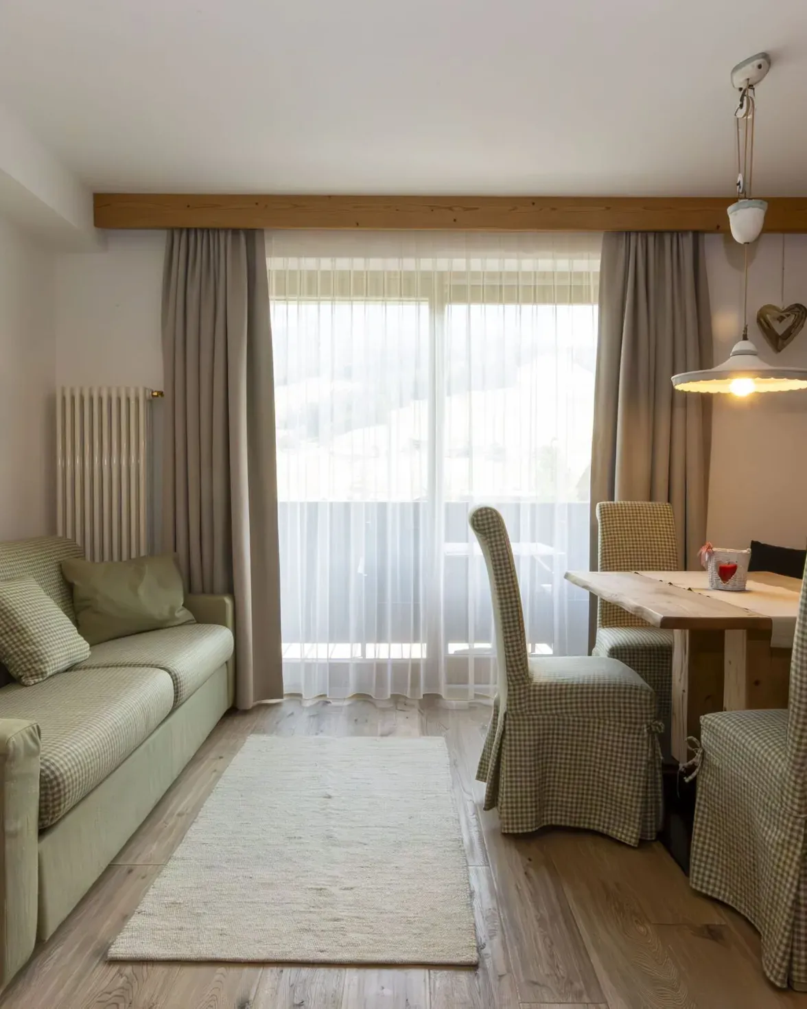 Cozy living and dining area with plaid sofa, wooden walls, and a dining table by a large window.