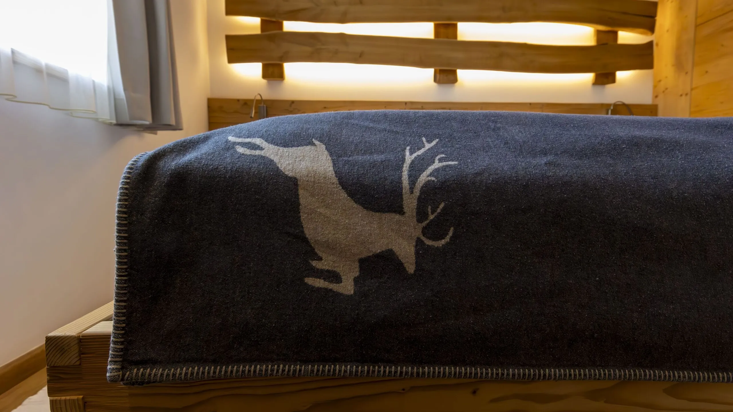 Cozy hotel bedroom with a dark blue blanket featuring a light-colored deer silhouette draped over a wooden bed.