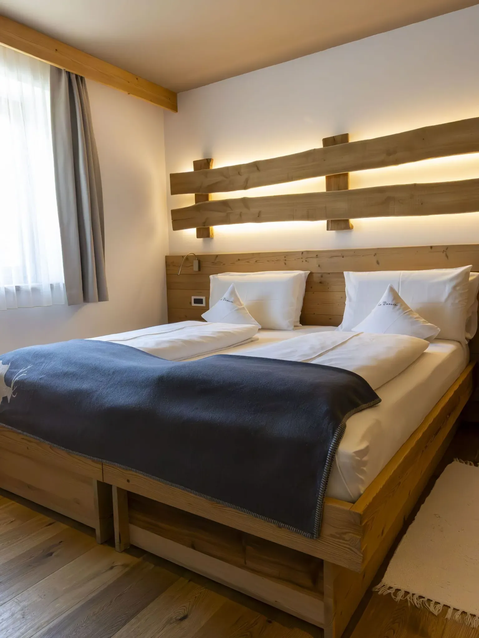 Cozy wooden hotel room with a large bed, white linens, and a backlit wooden headboard.