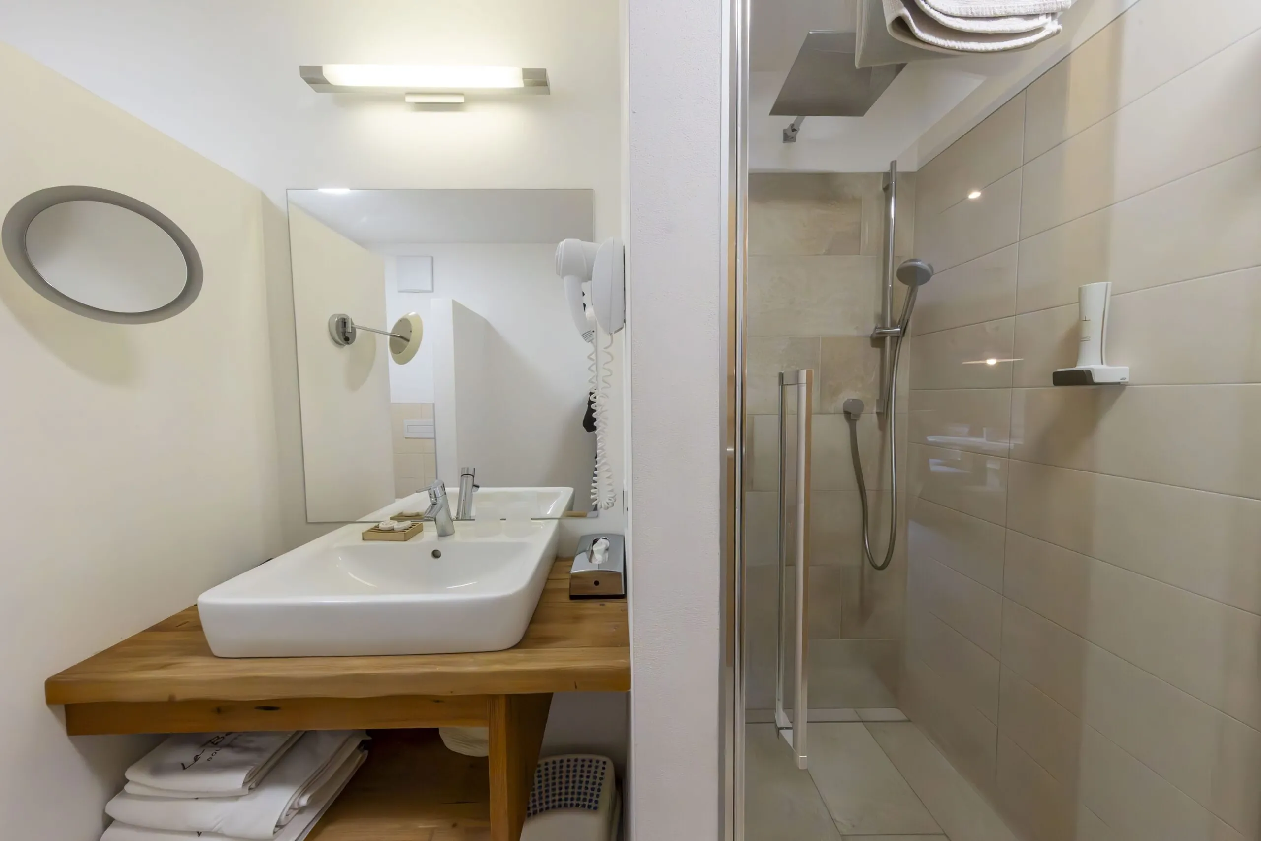 Bathroom with a wooden counter sink, wall mirror, hair dryer, and glass shower enclosure.