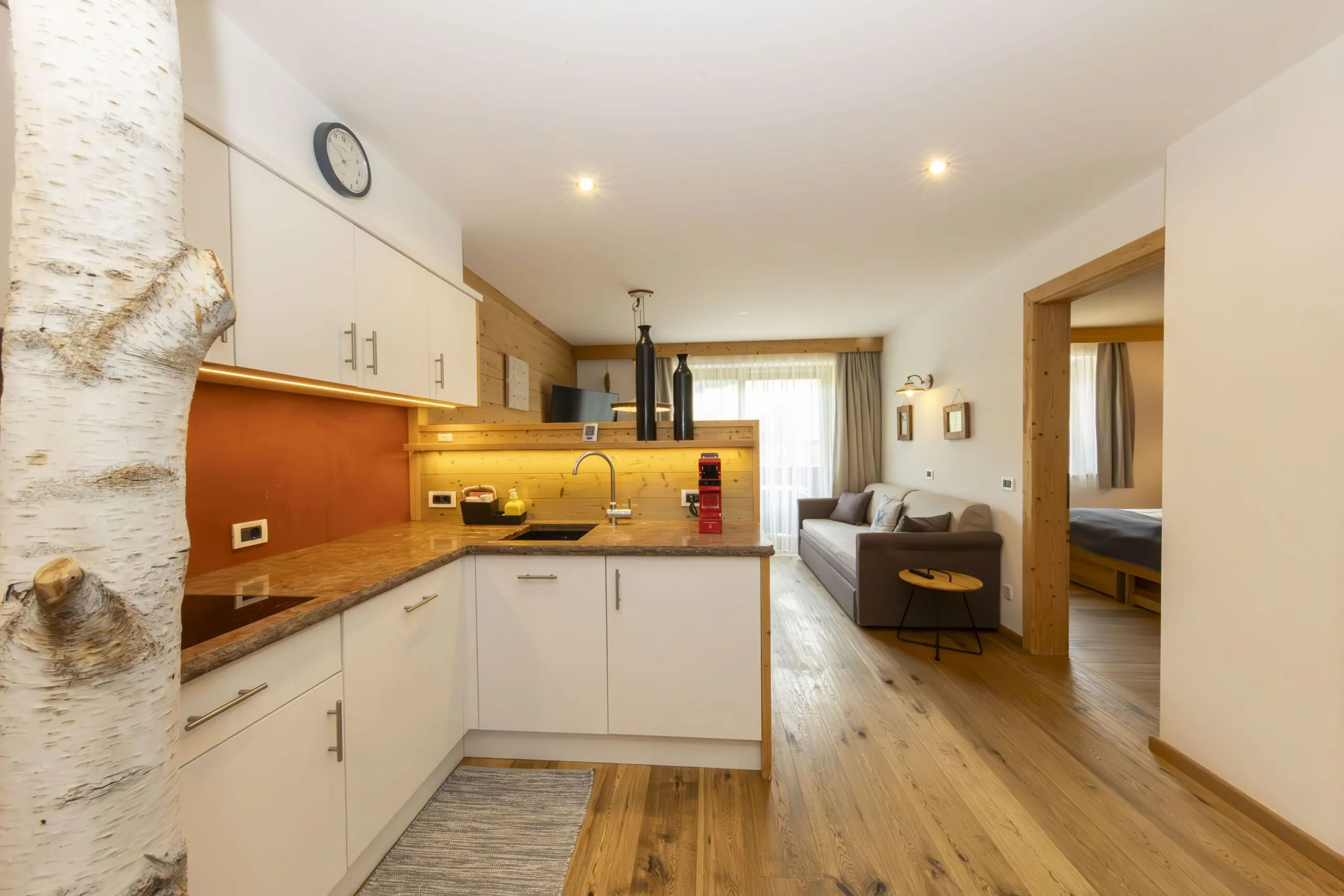 Open-plan kitchen with white cabinets, wooden countertops, and a living area featuring a gray sofa and natural wood accents.