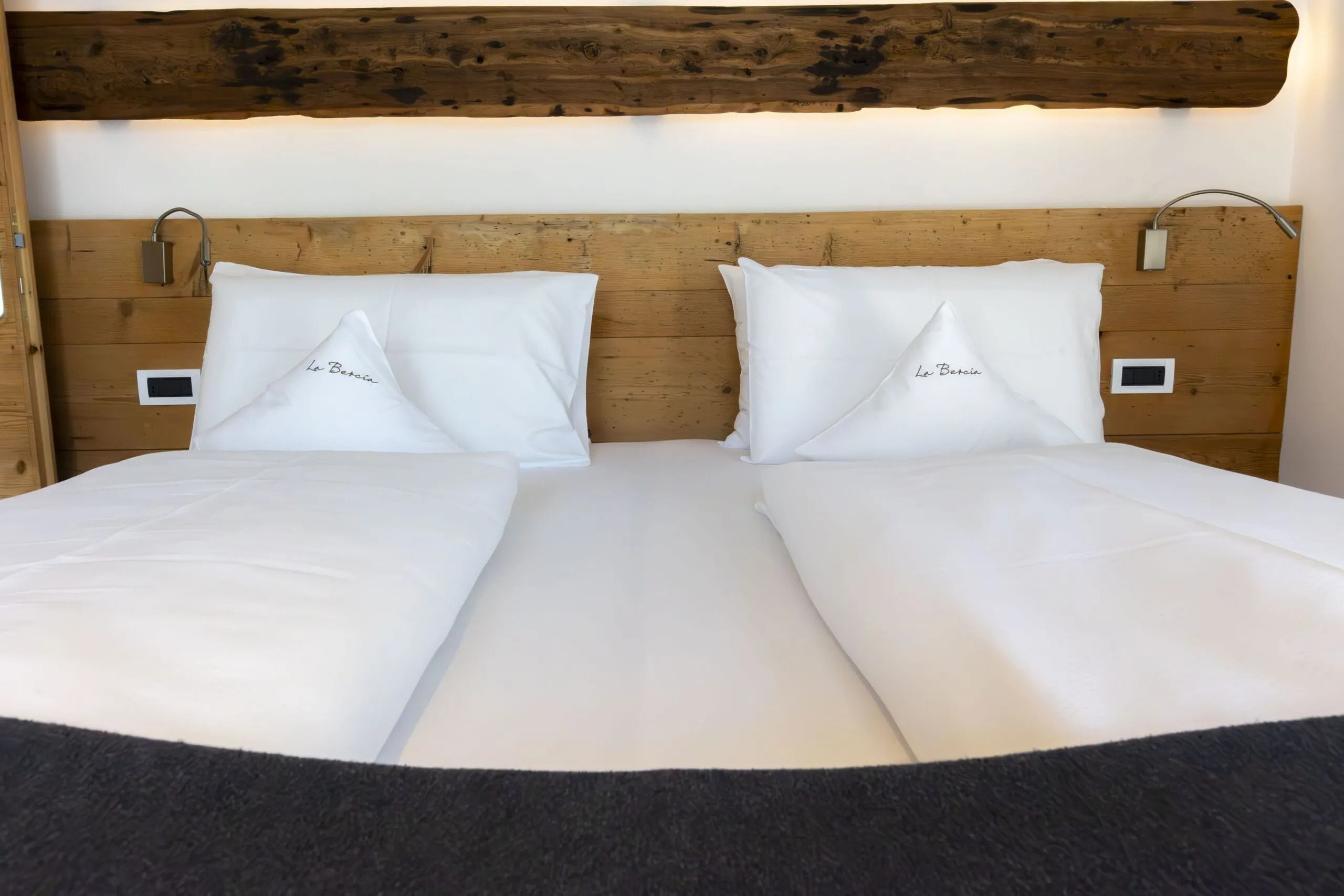Twin beds with white linens and embroidered pillows in a wooden headboard hotel room.