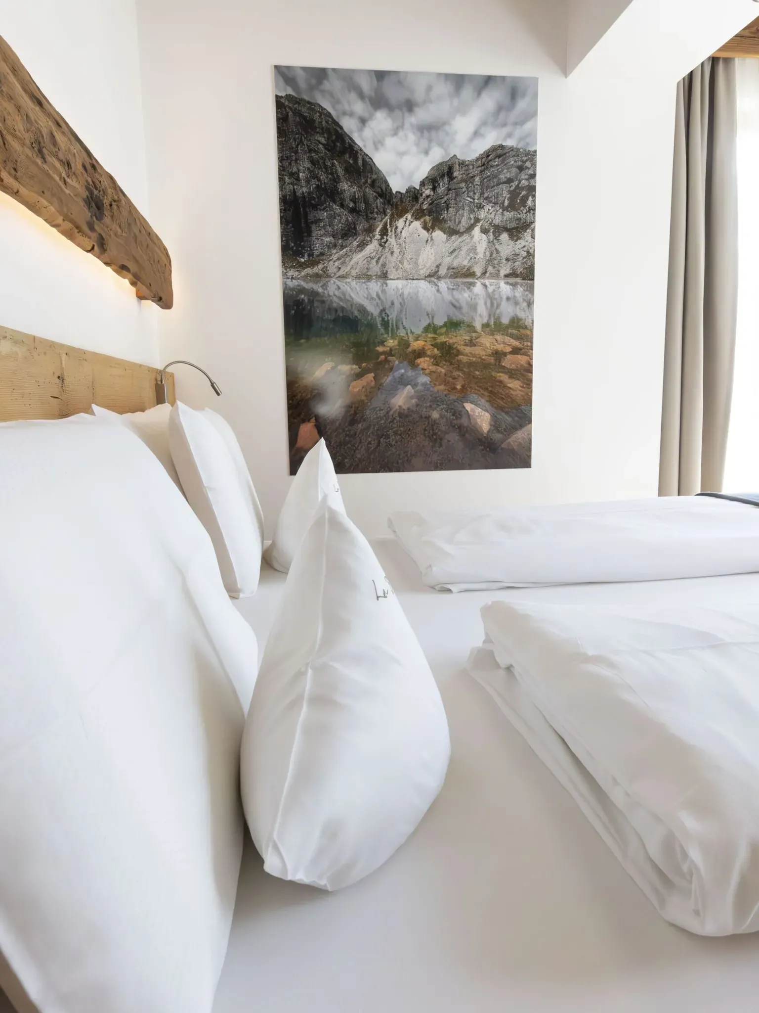 White-walled hotel room with a large landscape photo, white bedding, pillows, and a wooden headboard.