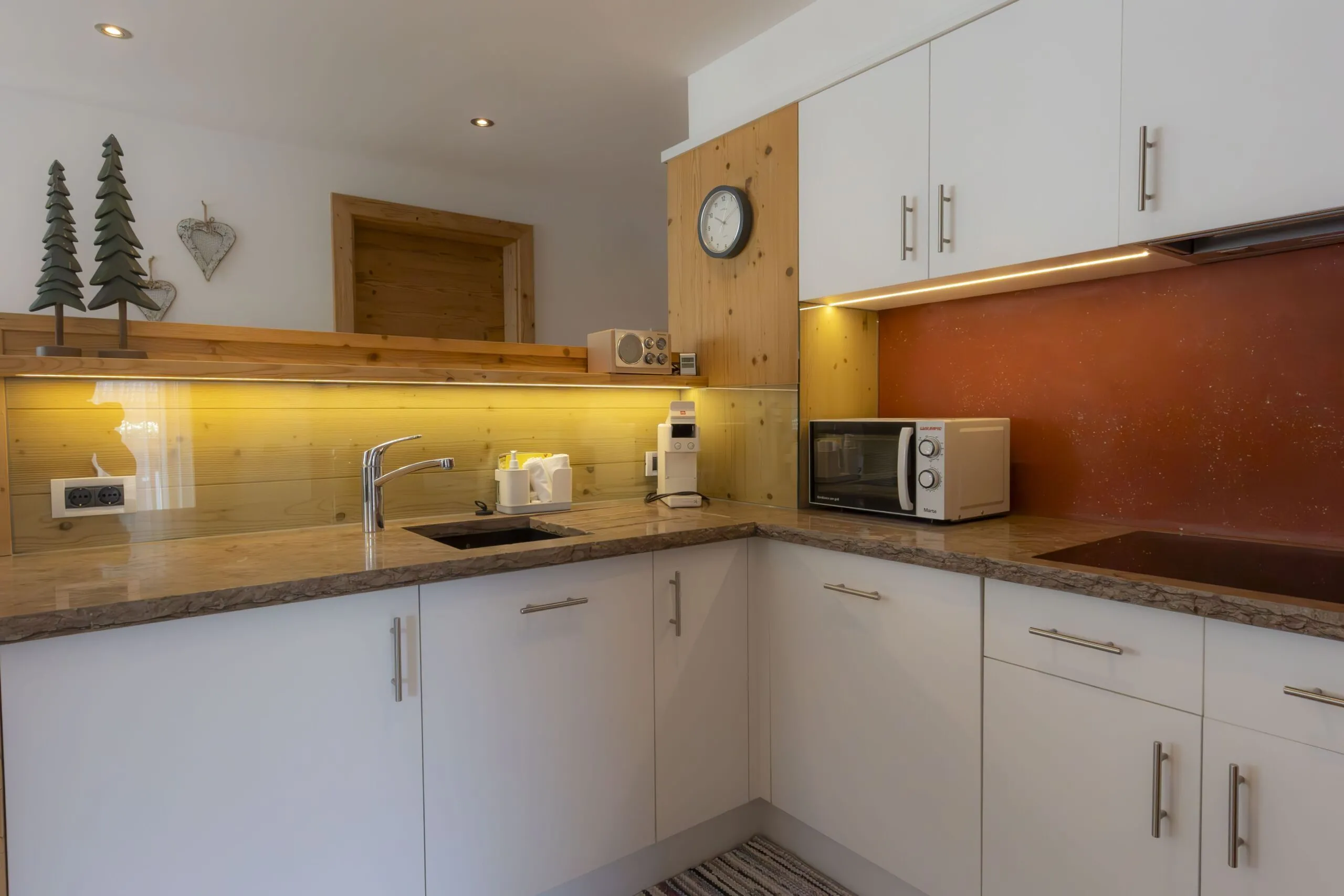 Cozy modern kitchen with white cabinets, marble-like countertops, warm wood accents, and small appliances.