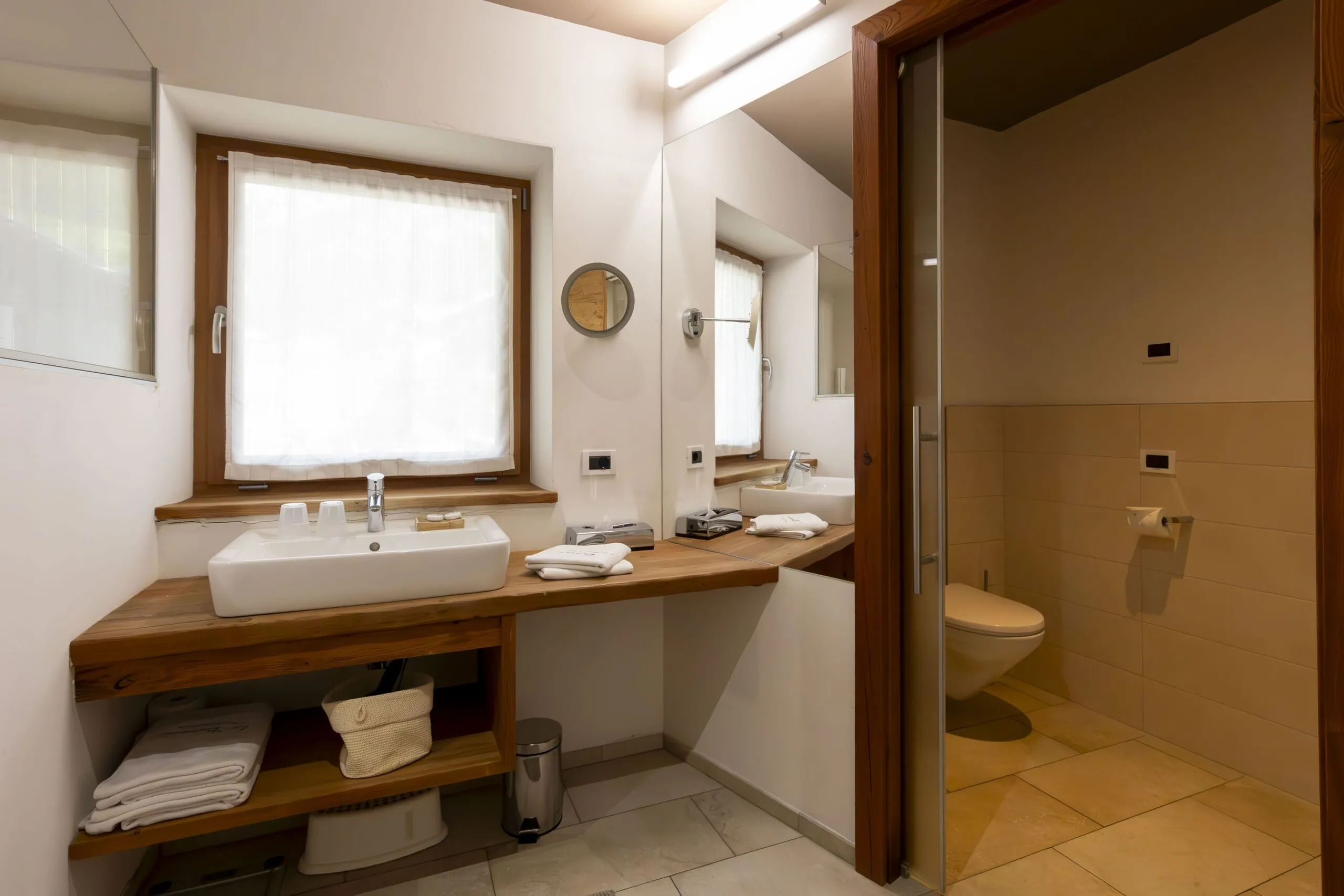 Wooden bathroom counter with sink, towels, mirror, window, and an adjacent enclosed toilet area.