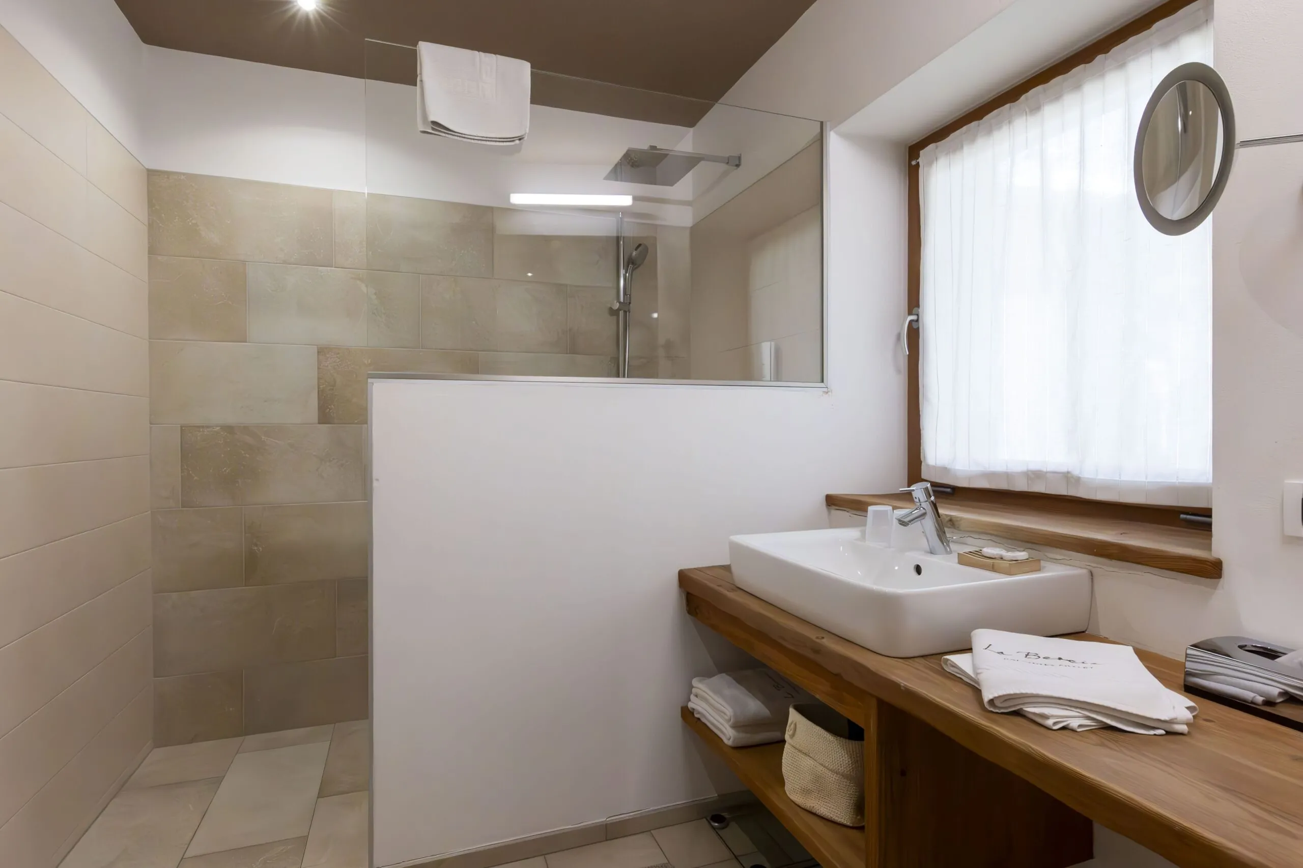 Bathroom with a wooden vanity, rectangular sink, towel, and a glass-walled shower in soft beige tones.