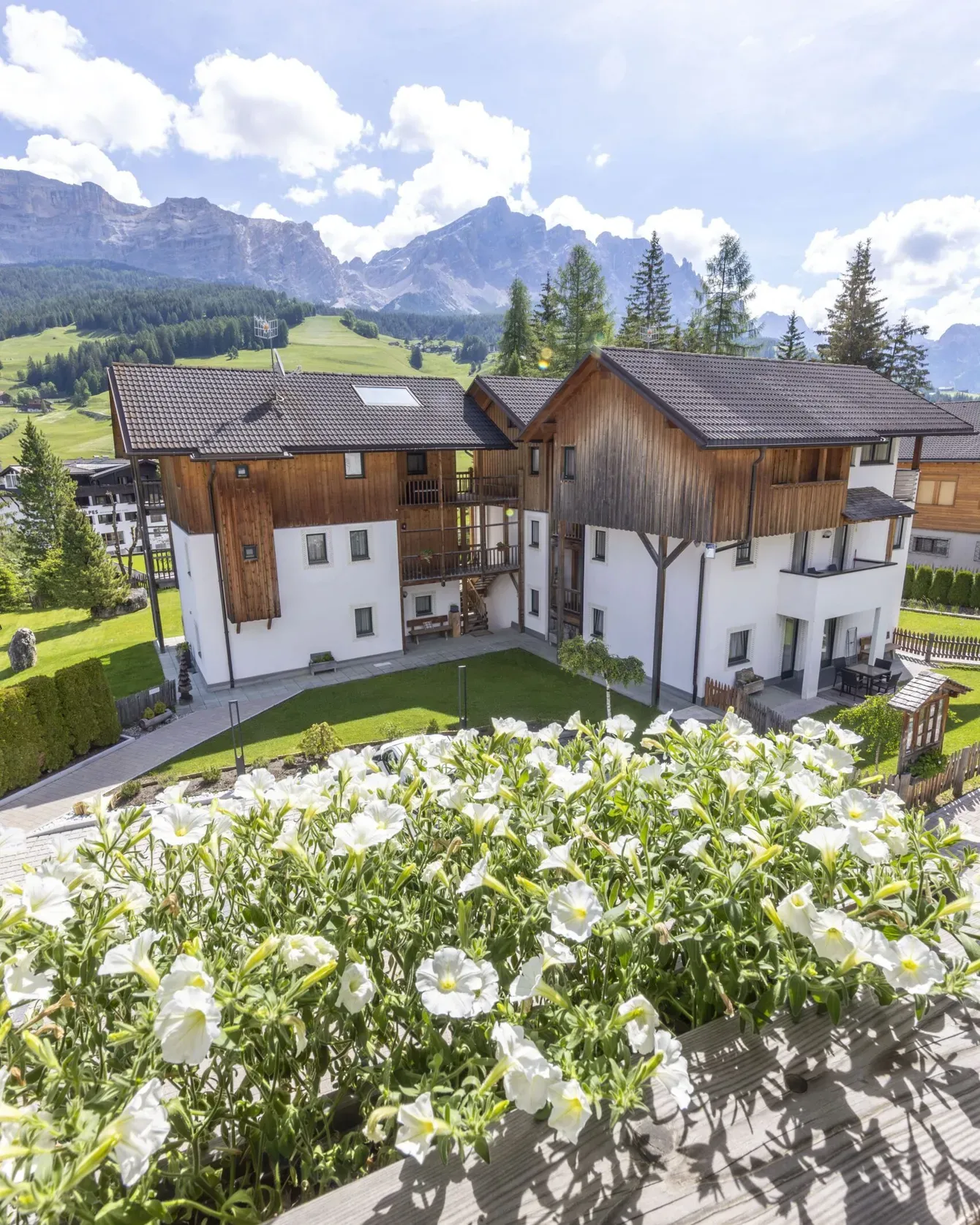 Charming mountain village with white-walled houses, wooden roofs, and blooming foreground flowers, alpine backdrop.