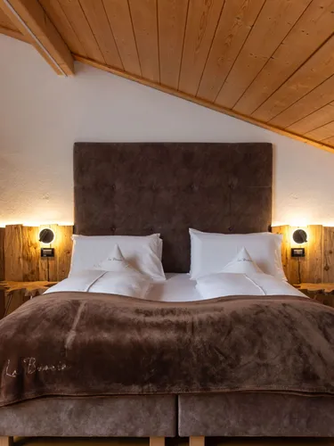 Cozy wooden loft bedroom with a plush brown bed, matching headboard, and warm bedside lamps.