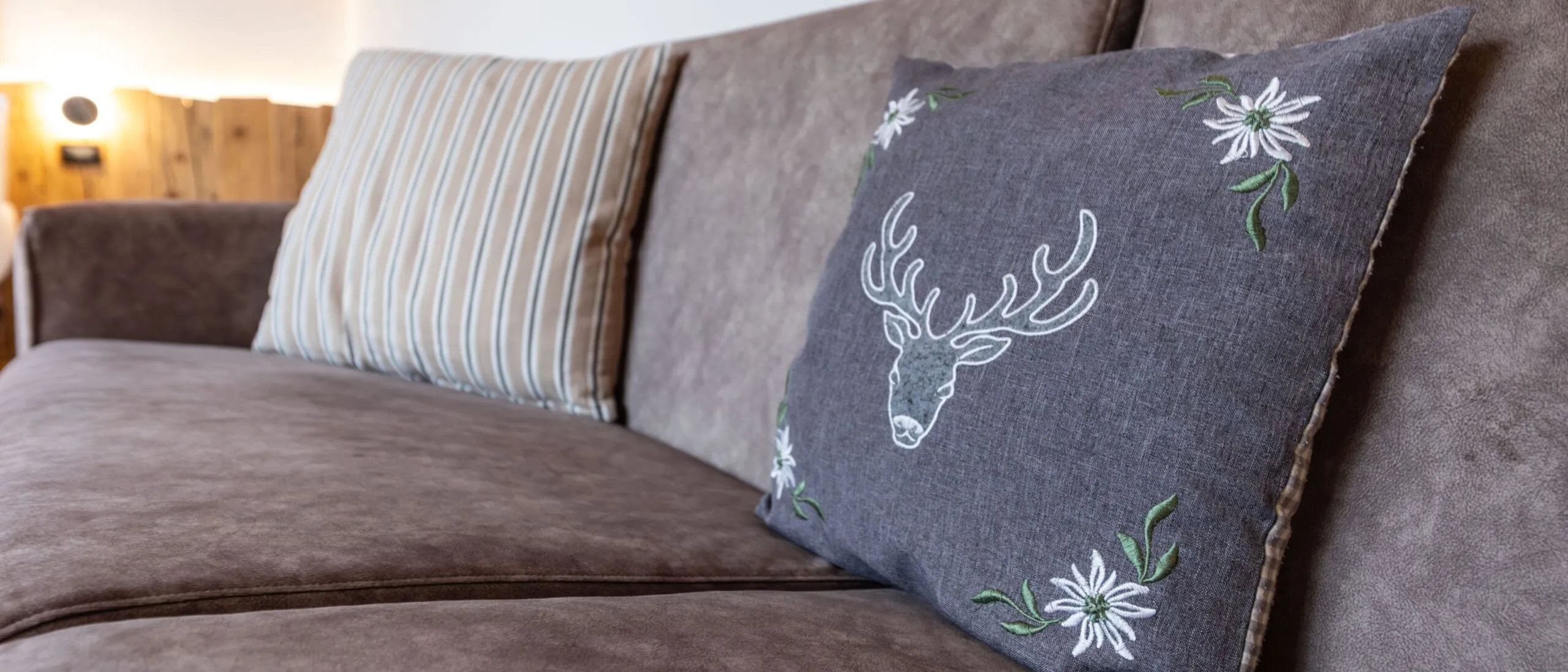 Soft brown couch with striped and dark gray embroidered cushions in a cozy room corner.