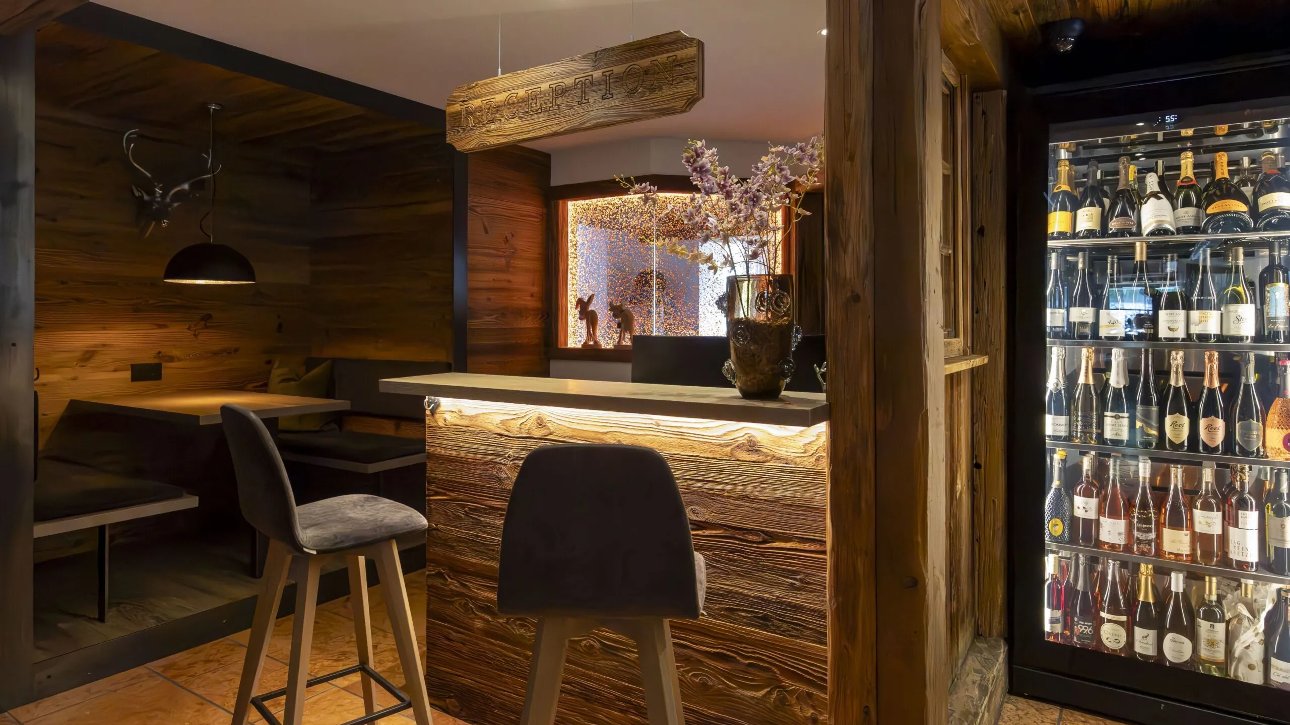 Cozy wood-paneled hotel reception area with a lit bar counter, high stool seating, and a glass-fronted wine fridge.