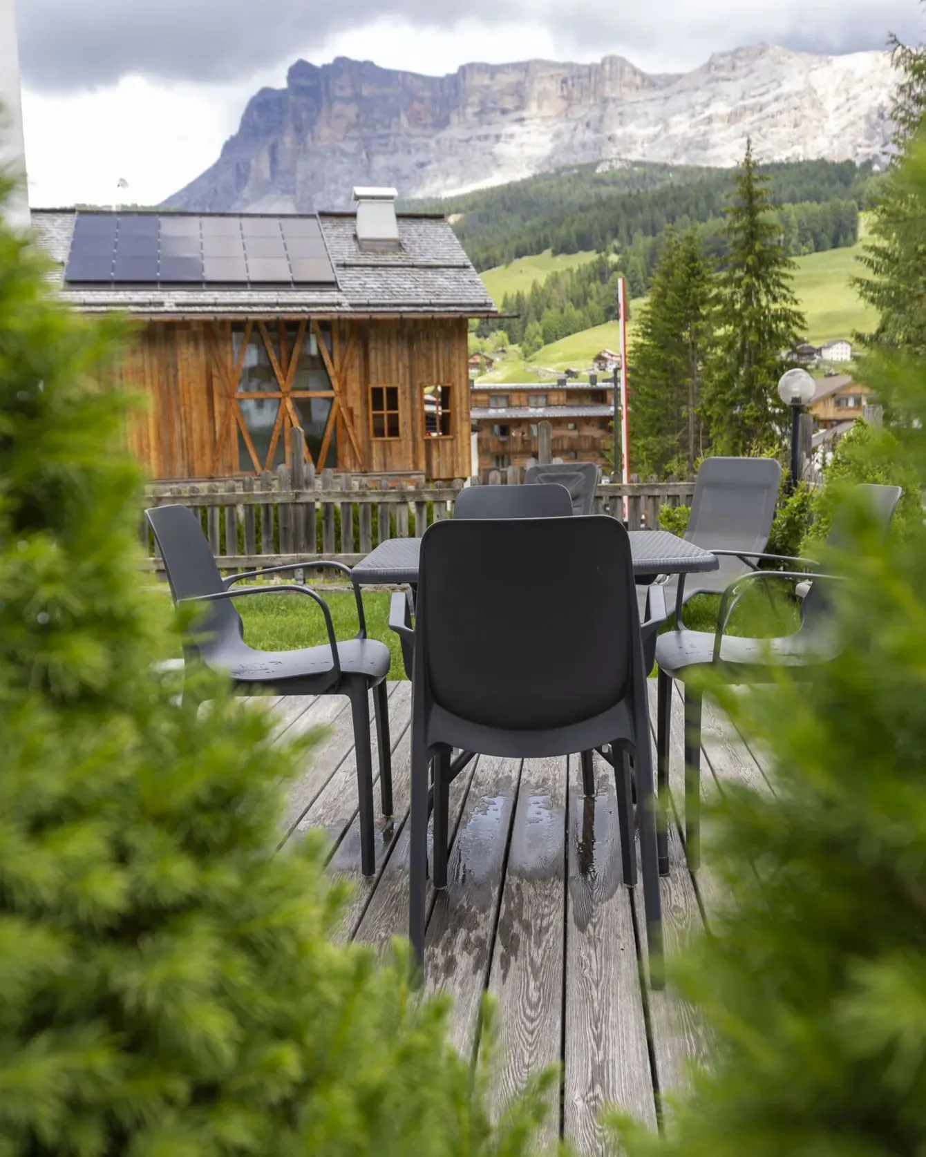 Outdoor wooden terrace with gray chairs and table, rustic cabin, green hills, and mountains in the background.