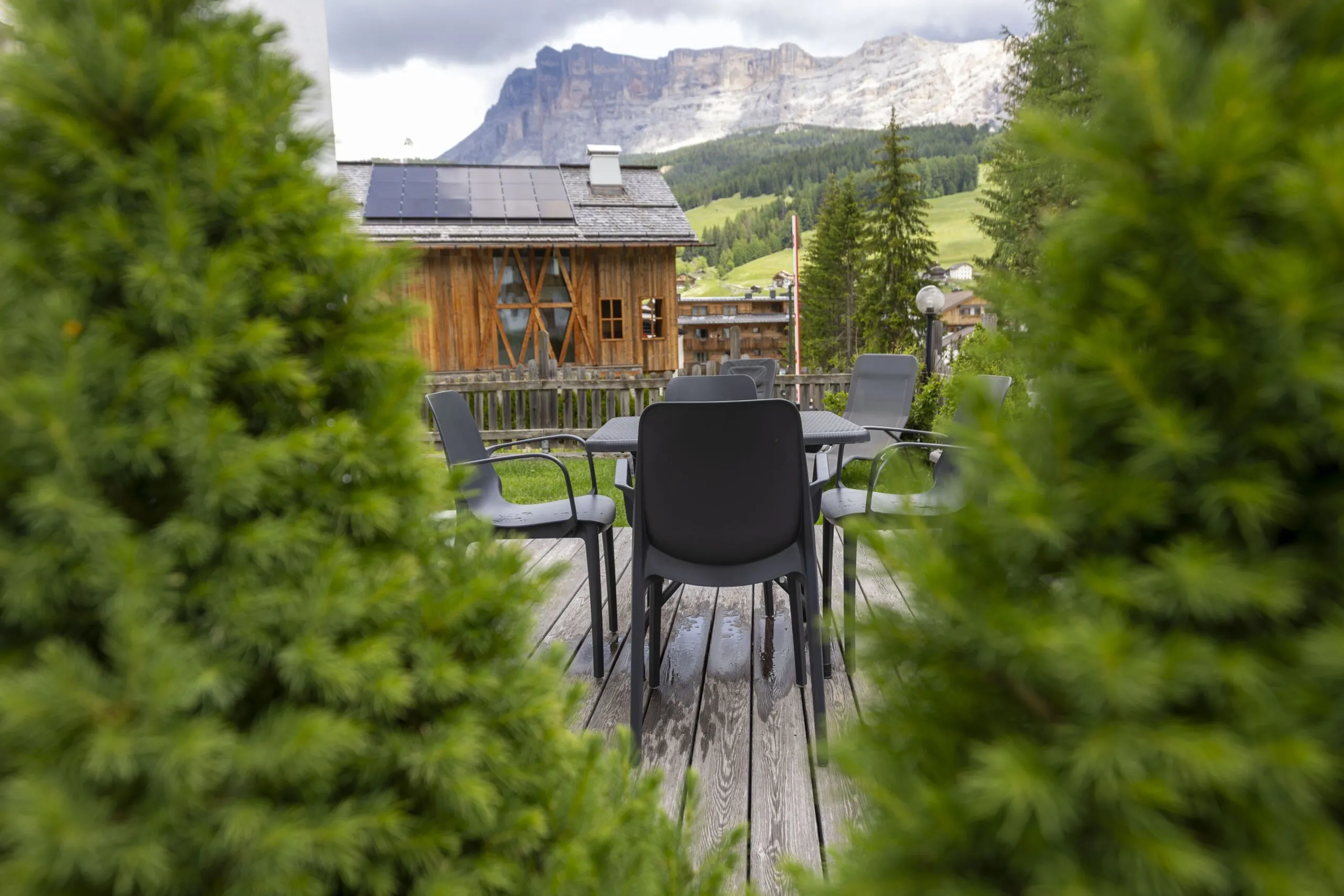 Outdoor wooden terrace with gray chairs and table, rustic cabin, green hills, and mountains in the background.
