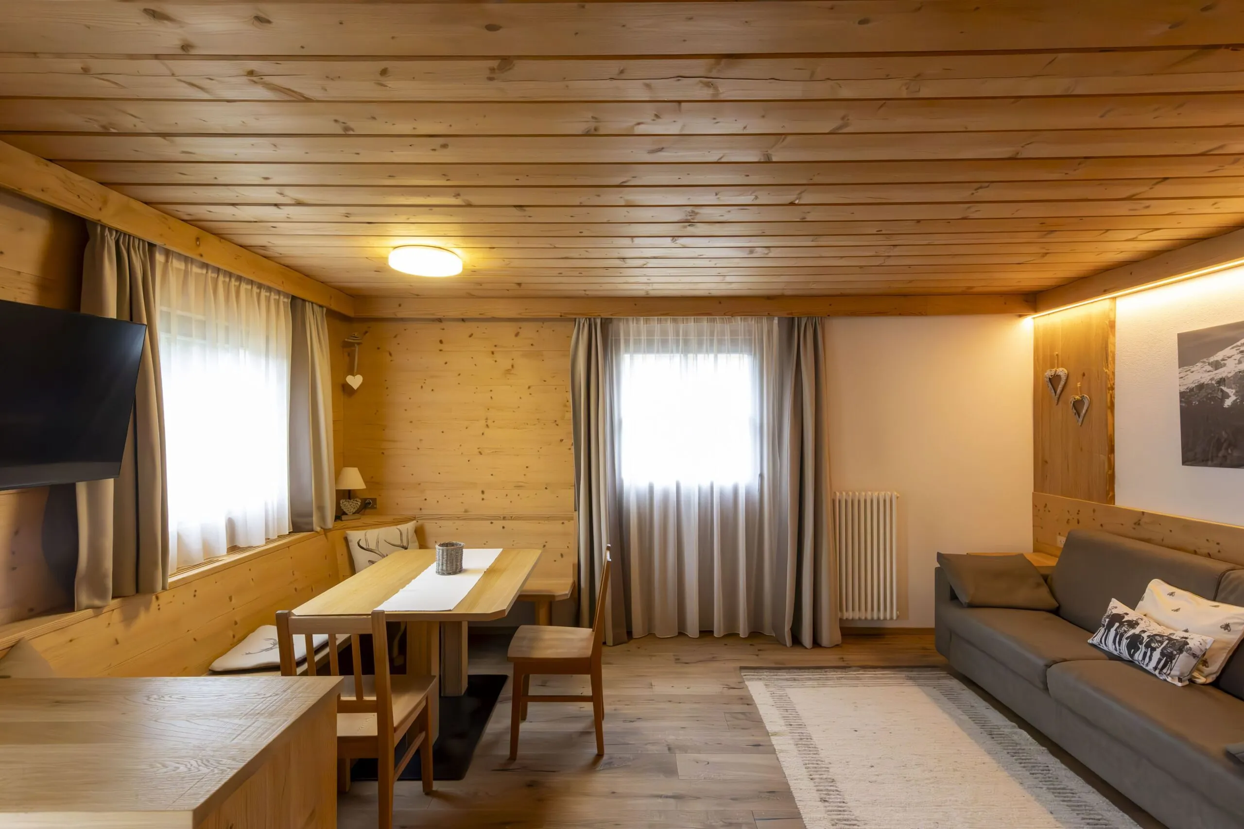 Cozy wood-paneled living room with sofa, dining table, chairs, and curtains in a rustic interior.