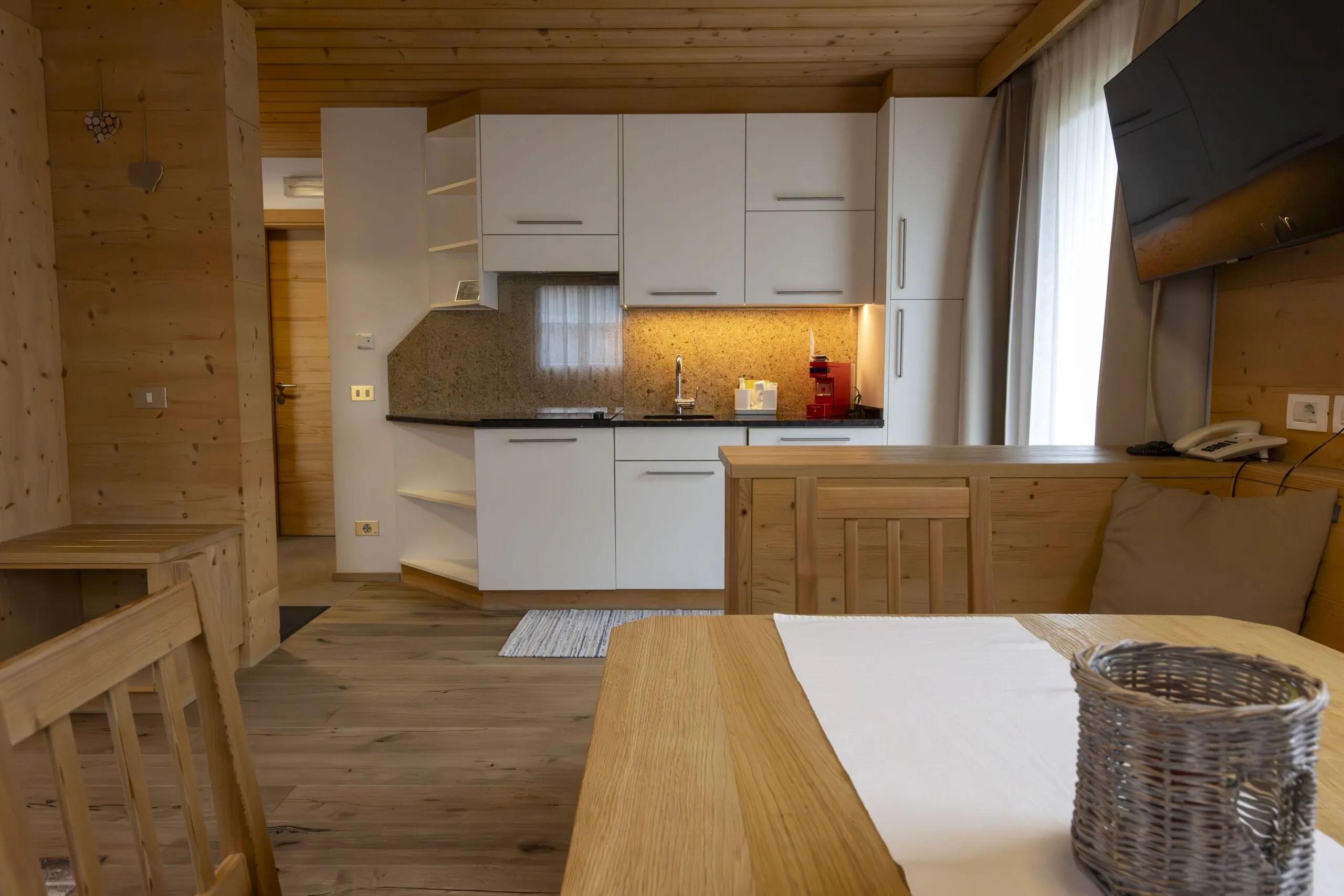 Cozy wooden kitchen and dining area with white cabinets, granite countertop, and a table with a basket centerpiece.