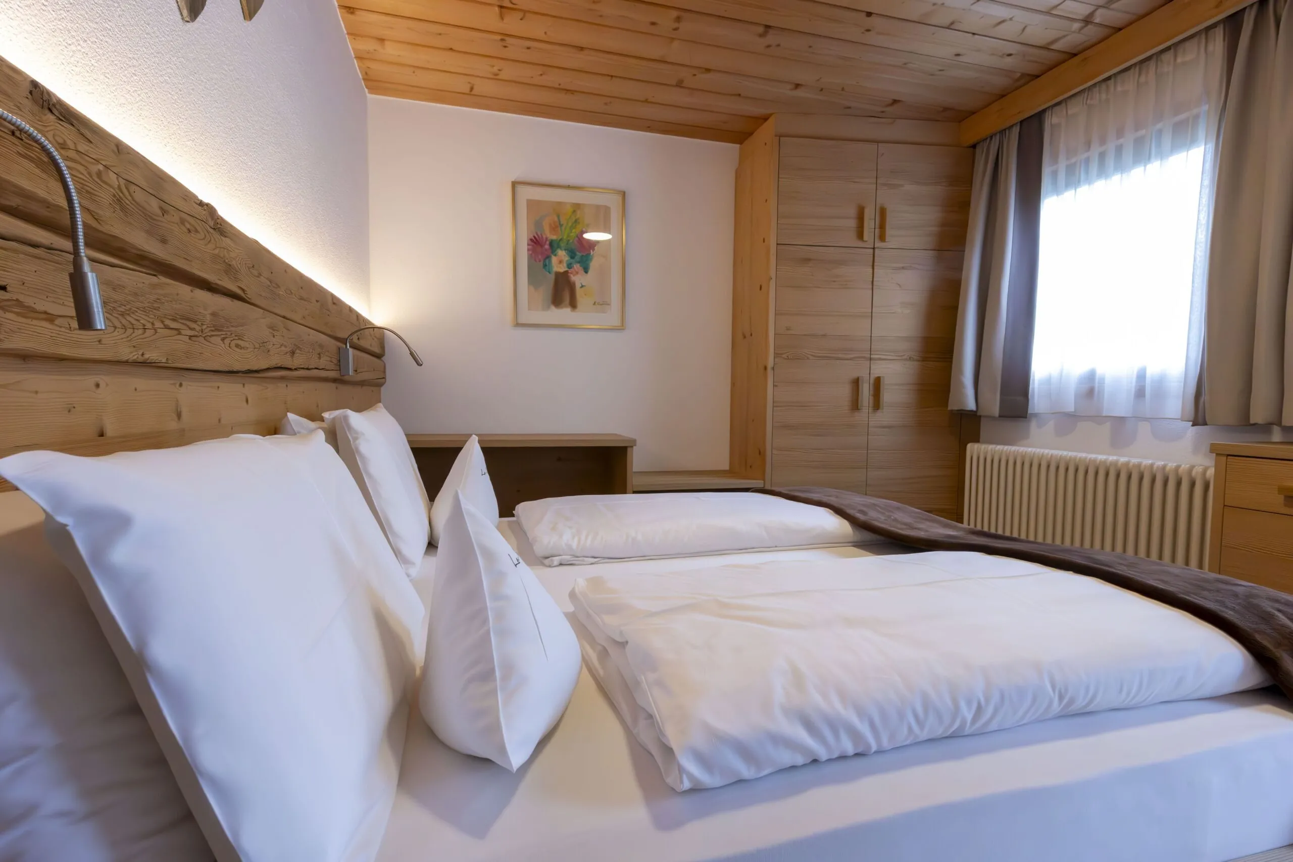 Twin beds with white linens in a cozy wood-paneled hotel room at La Villa, Alta Badia.