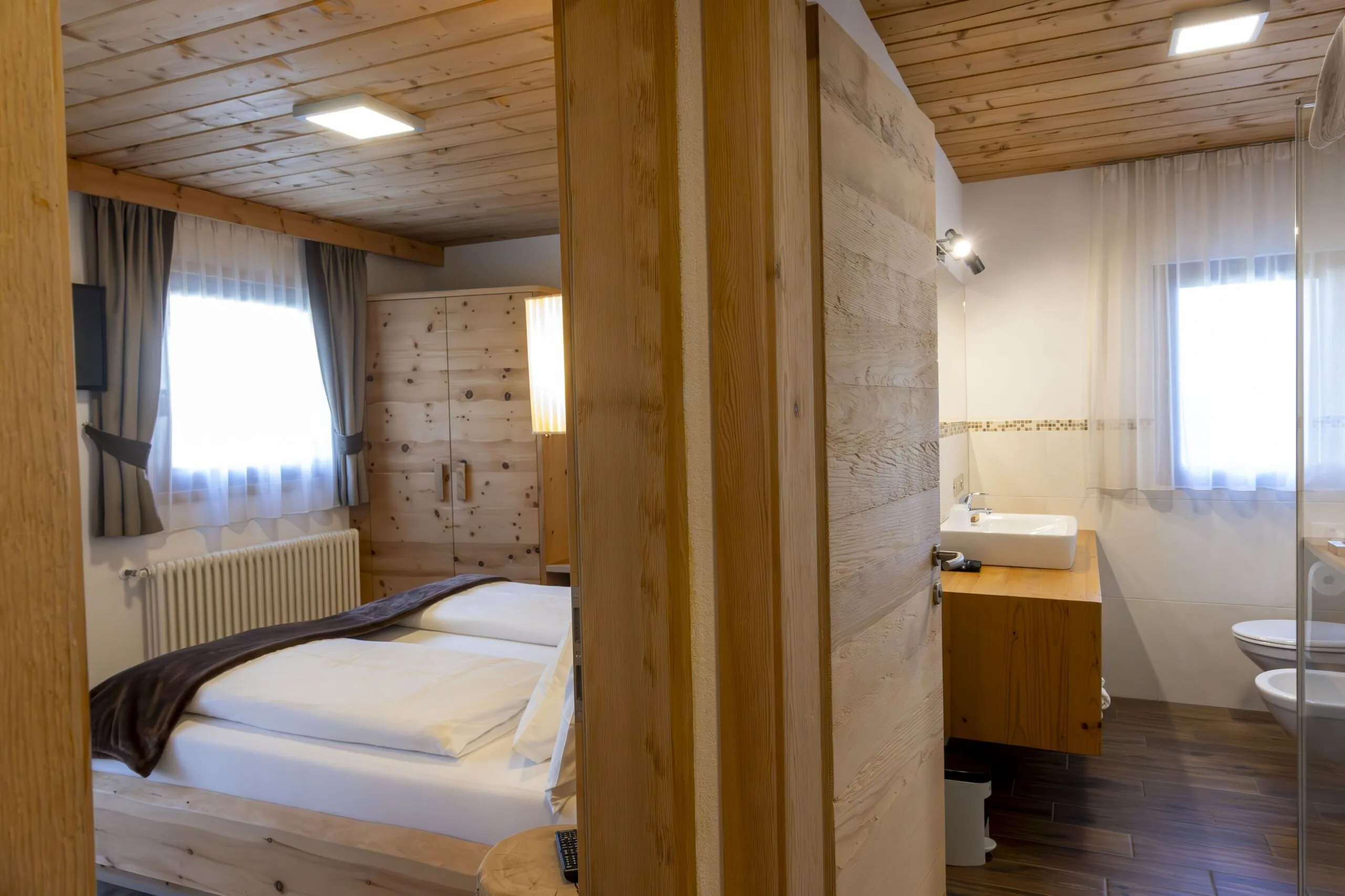Cozy wooden hotel room with double bed, wardrobe, and a connected bathroom area with sink and toilet.