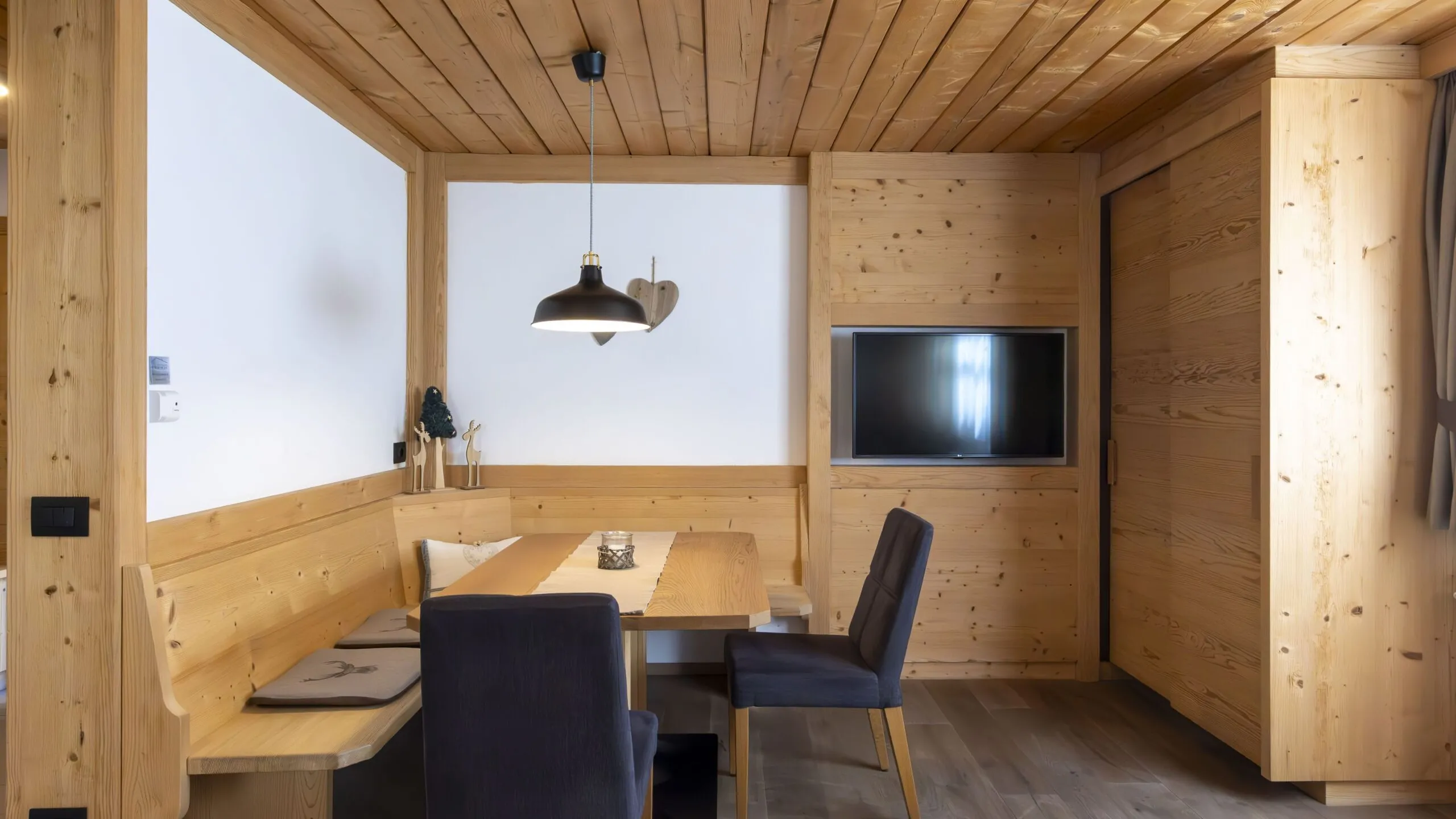 Cozy wooden dining nook with bench seating, a rectangular table, navy chairs, and a mounted flat-screen TV.