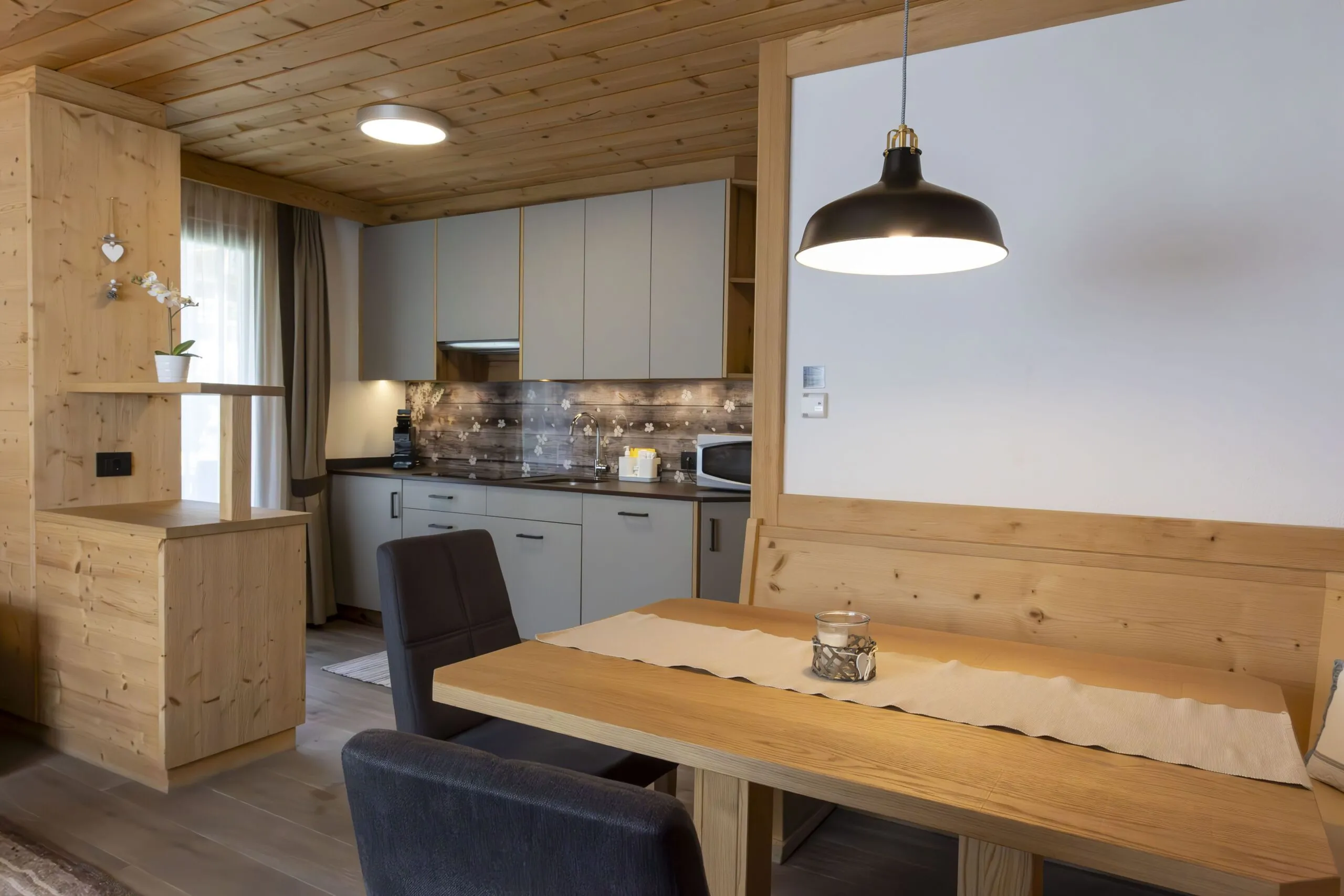 Cozy wooden kitchen and dining area with grey cabinets, black pendant light, and a wood dining table.