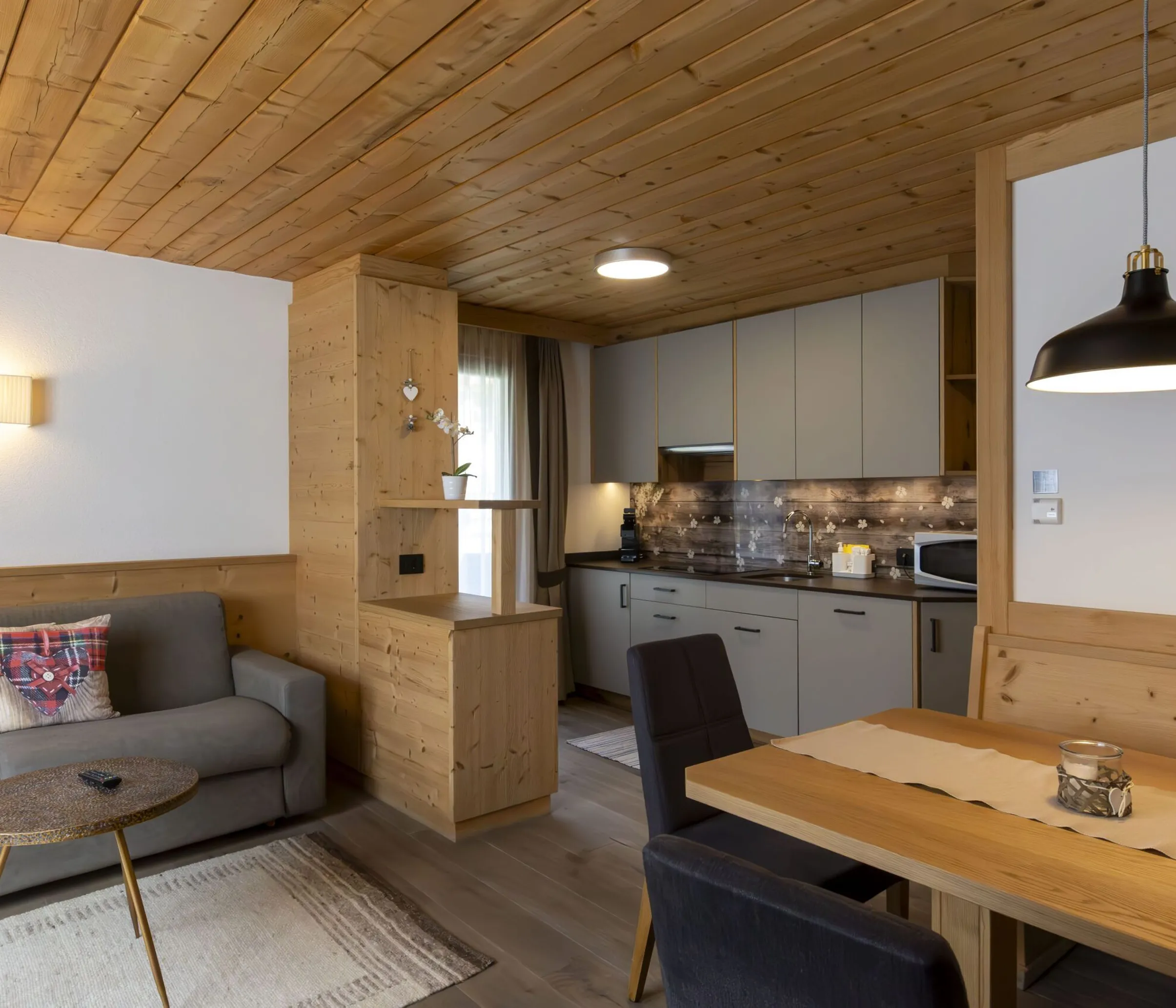 Cozy open-plan living room and kitchen in a wood-paneled cabin with gray sofa and dining table.