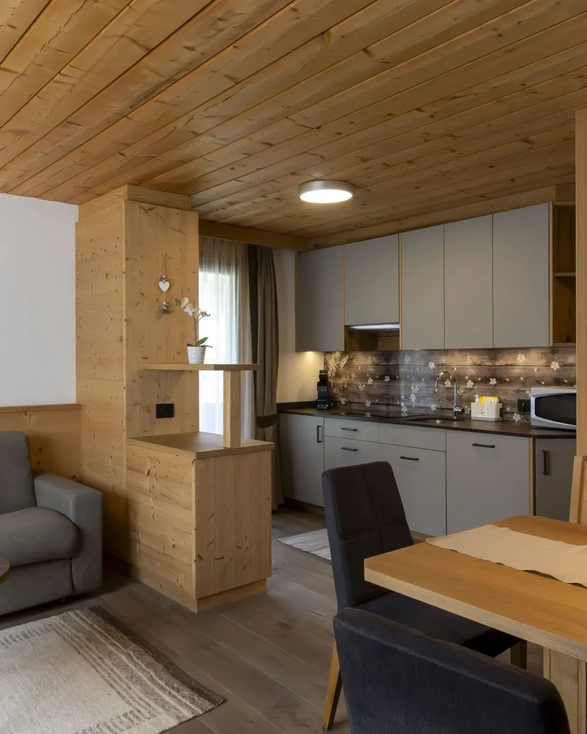 Cozy open-plan living room and kitchen in a wood-paneled cabin with gray sofa and dining table.