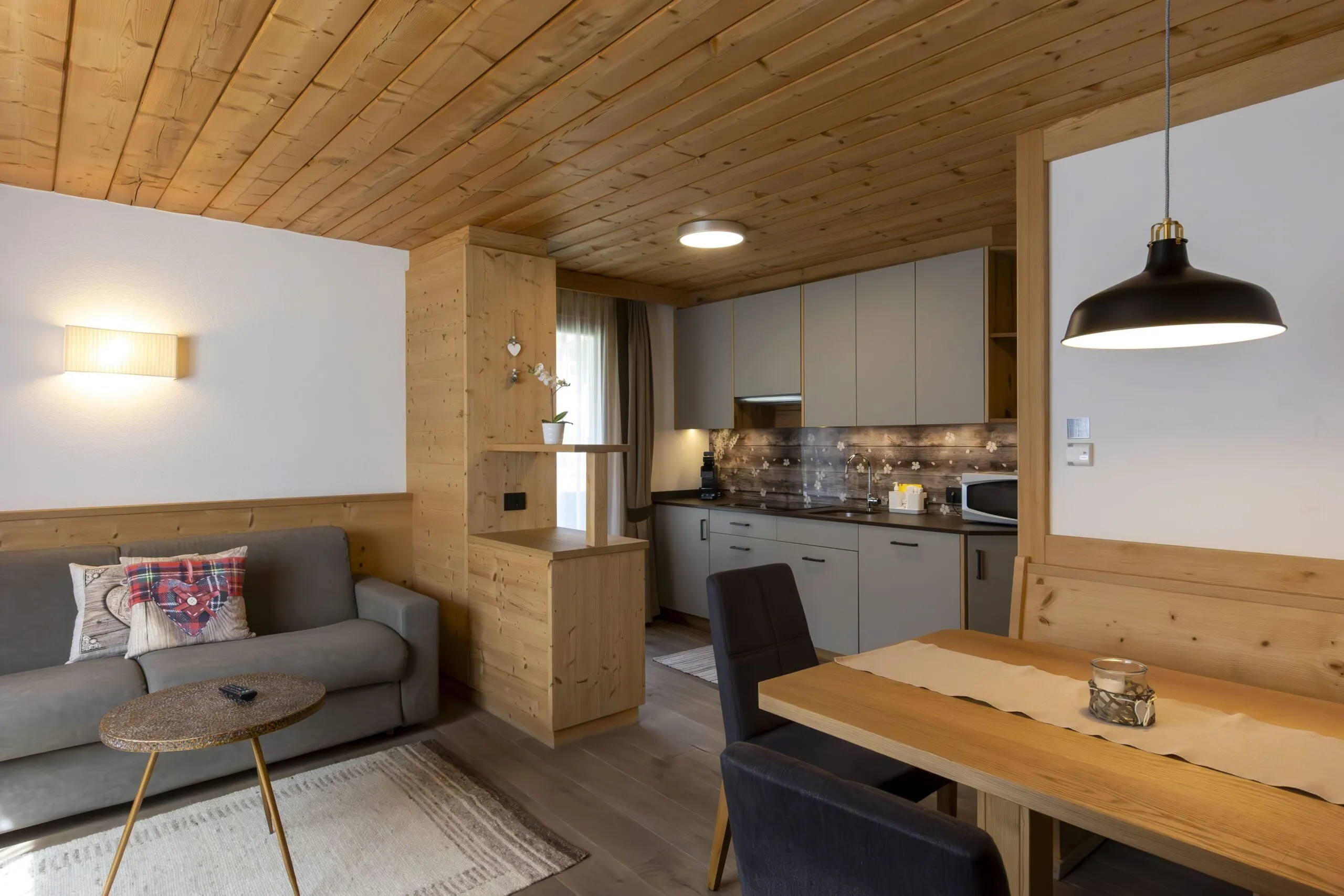 Cozy open-plan living room and kitchen in a wood-paneled cabin with gray sofa and dining table.