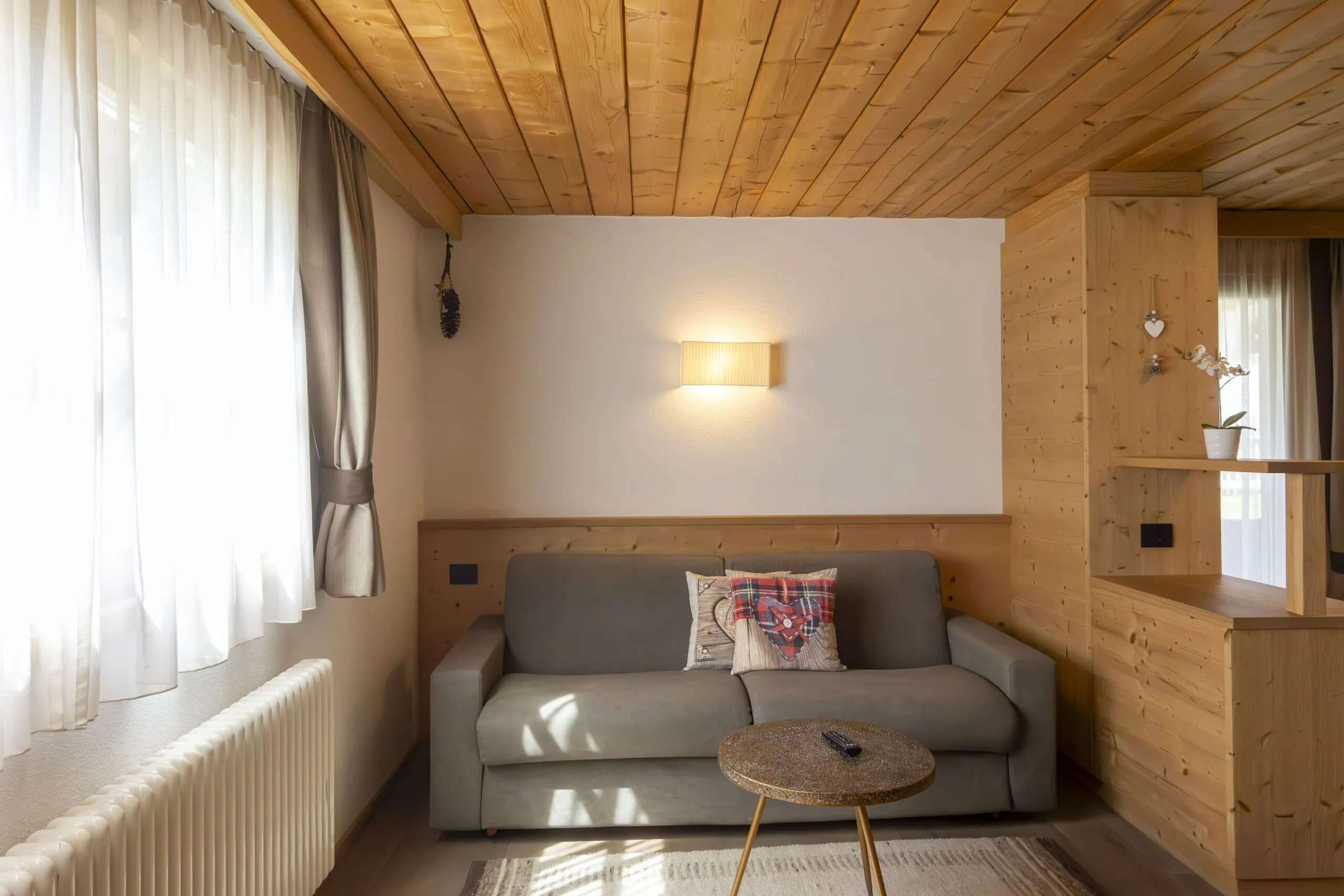 Cozy living room with a gray sofa, wooden panel walls, round coffee table, and warm wall light.
