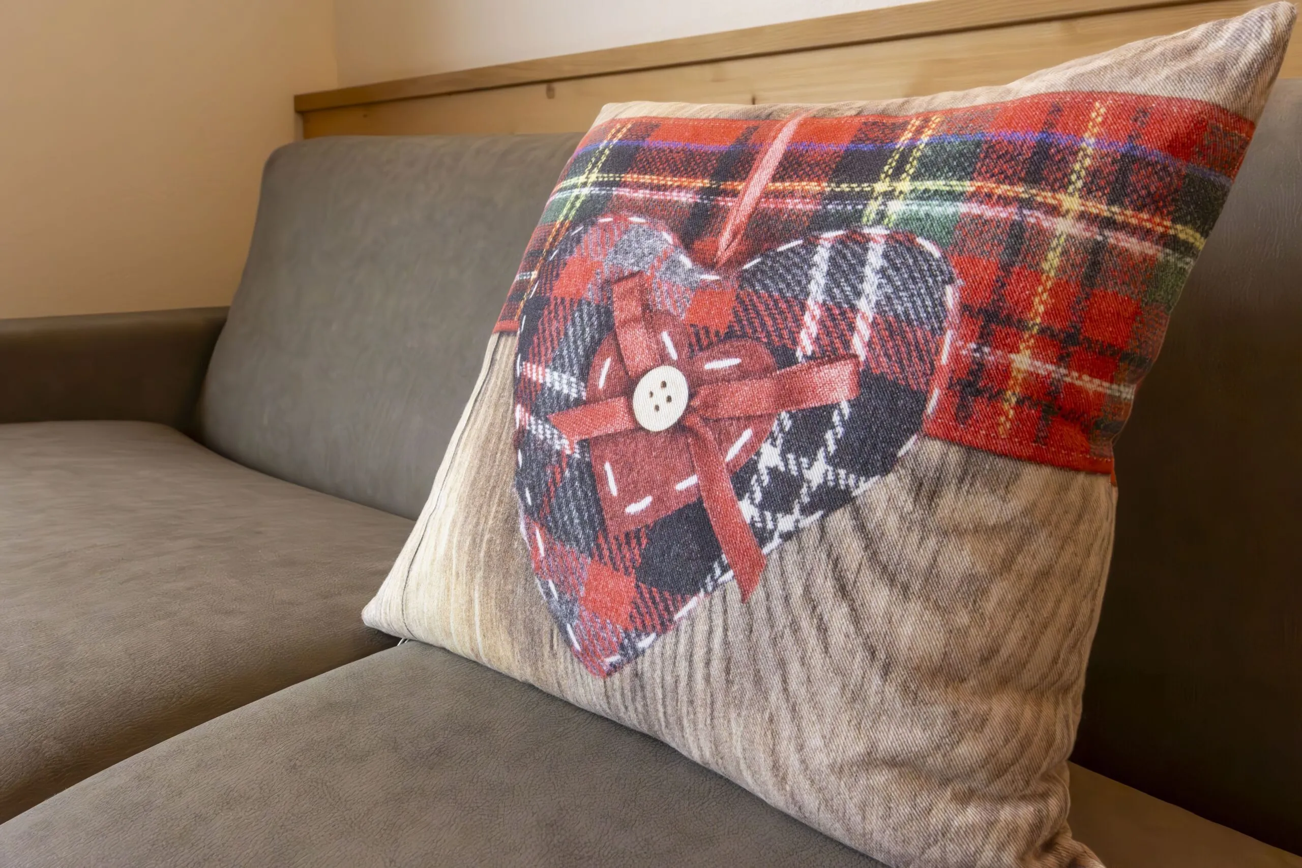 Decorative beige cushion with red plaid heart design and button, resting on a gray sofa.