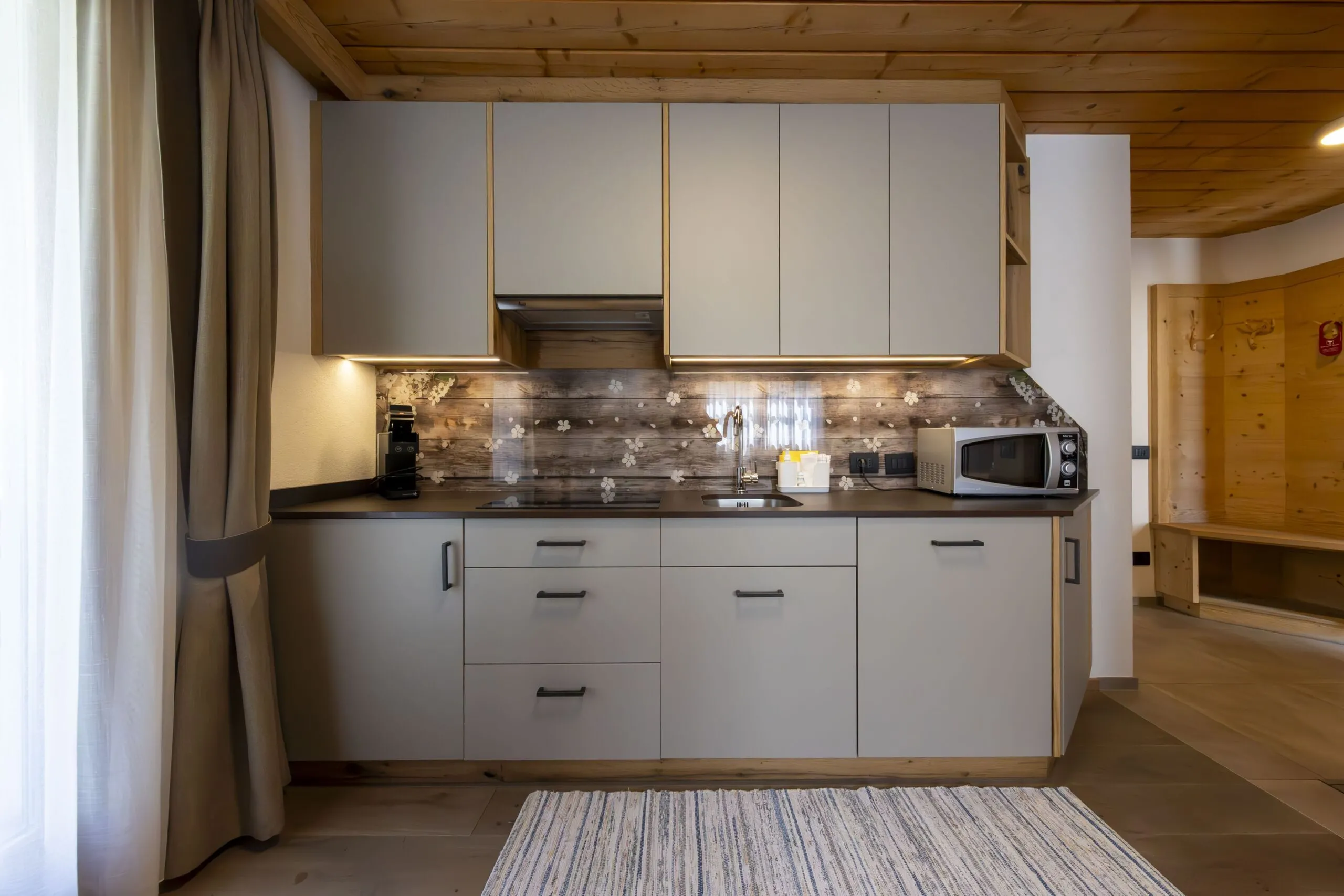 Modern gray kitchen with oak accents, under-cabinet lighting, and floral backsplash in a wooden-lodge interior.