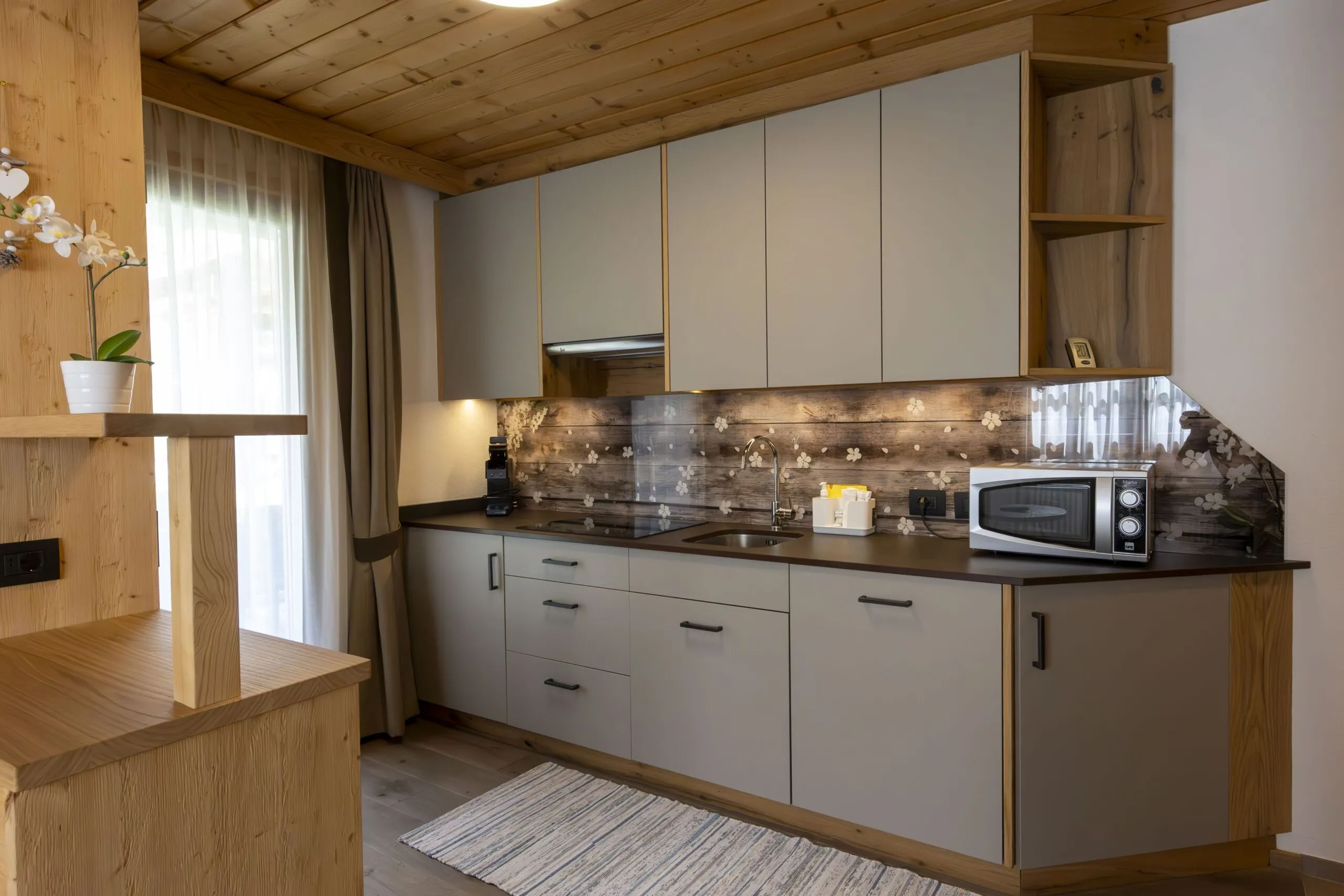 modern kitchen with gray cabinets, wooden accents, backsplash, sink, microwave, and small shelf area