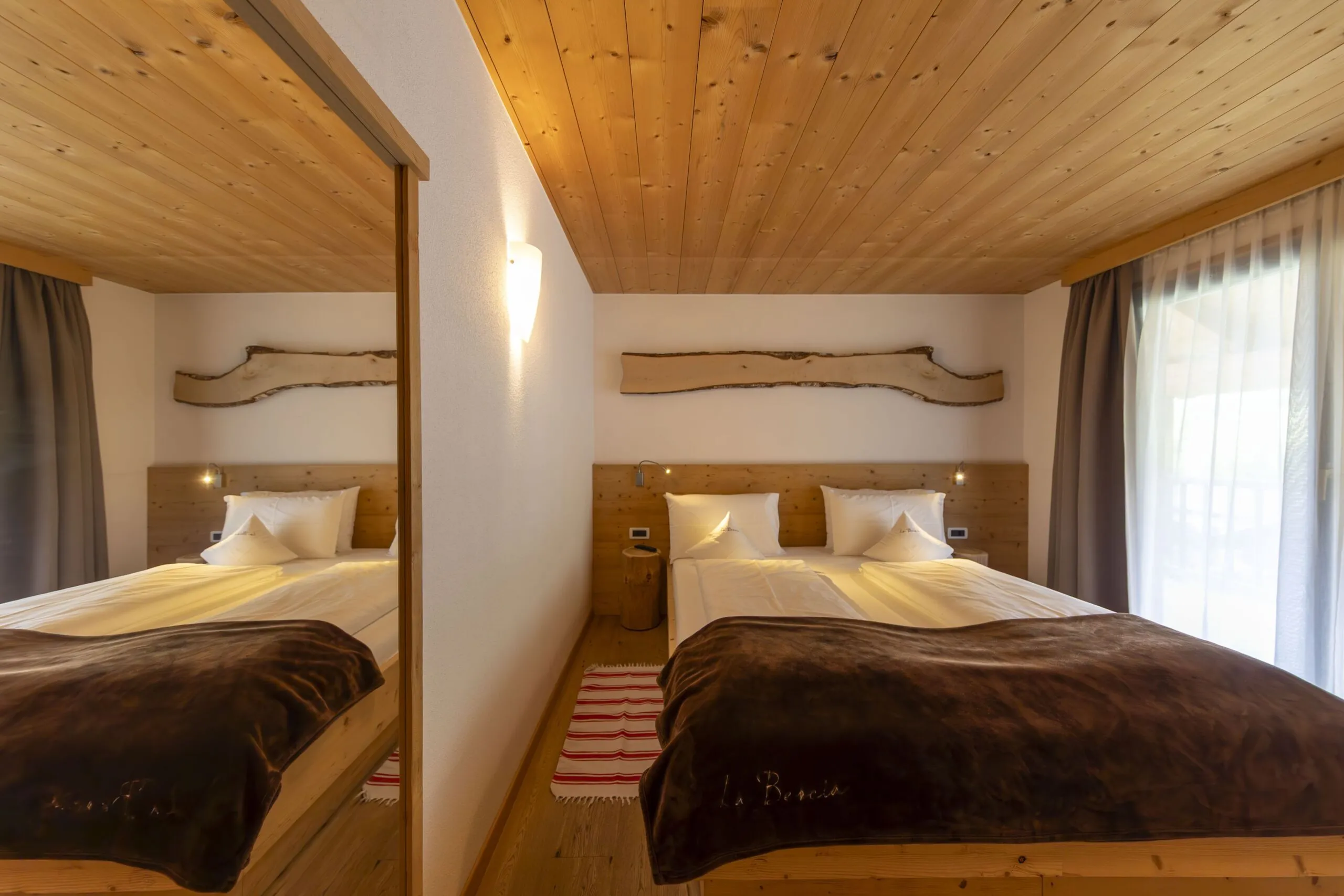 Cozy wooden hotel room with two single beds, warm lighting, and a large mirror reflecting the beds.