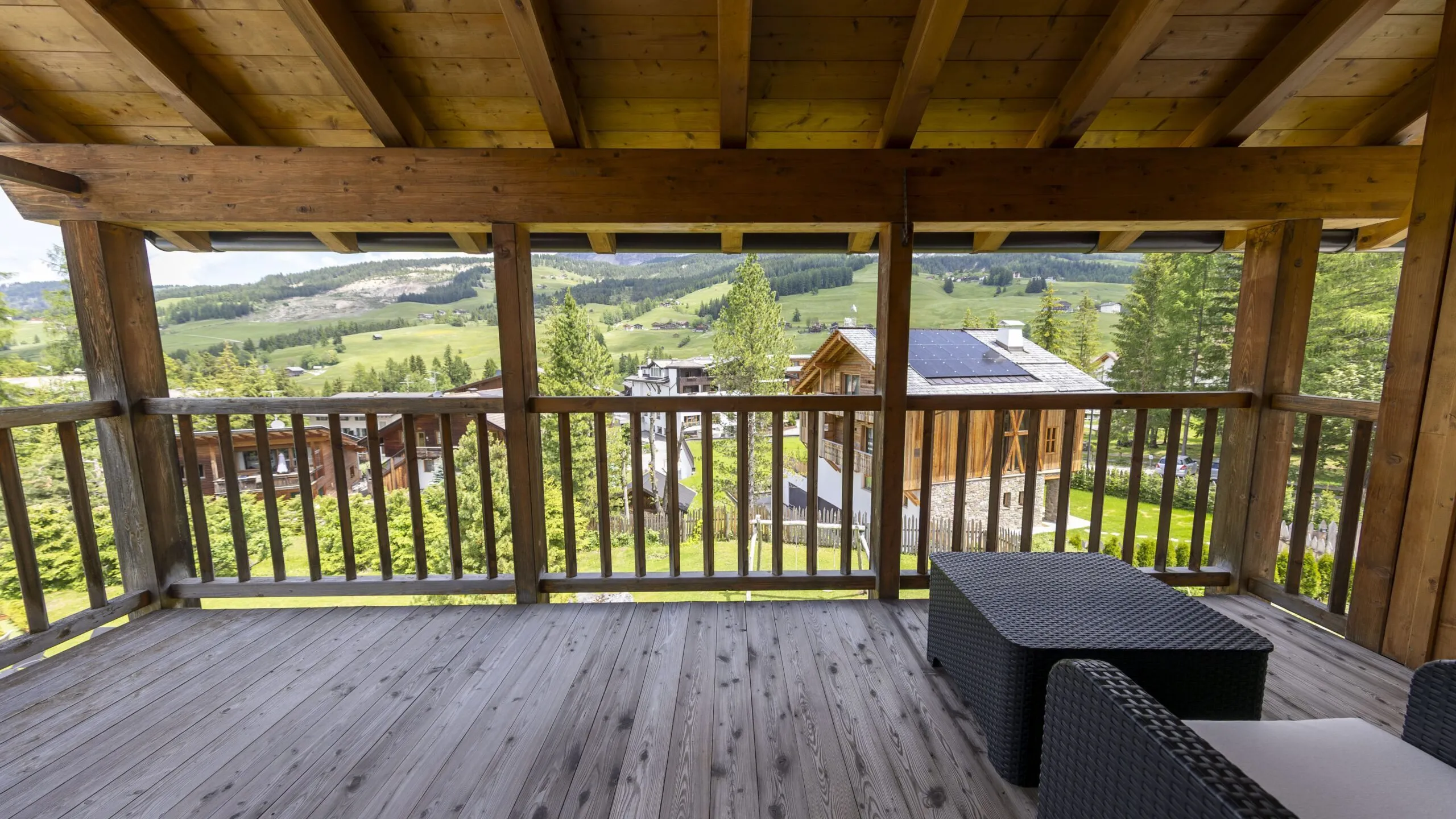 Wooden balcony with railing overlooking a green valley and wooden houses in a alpine village.