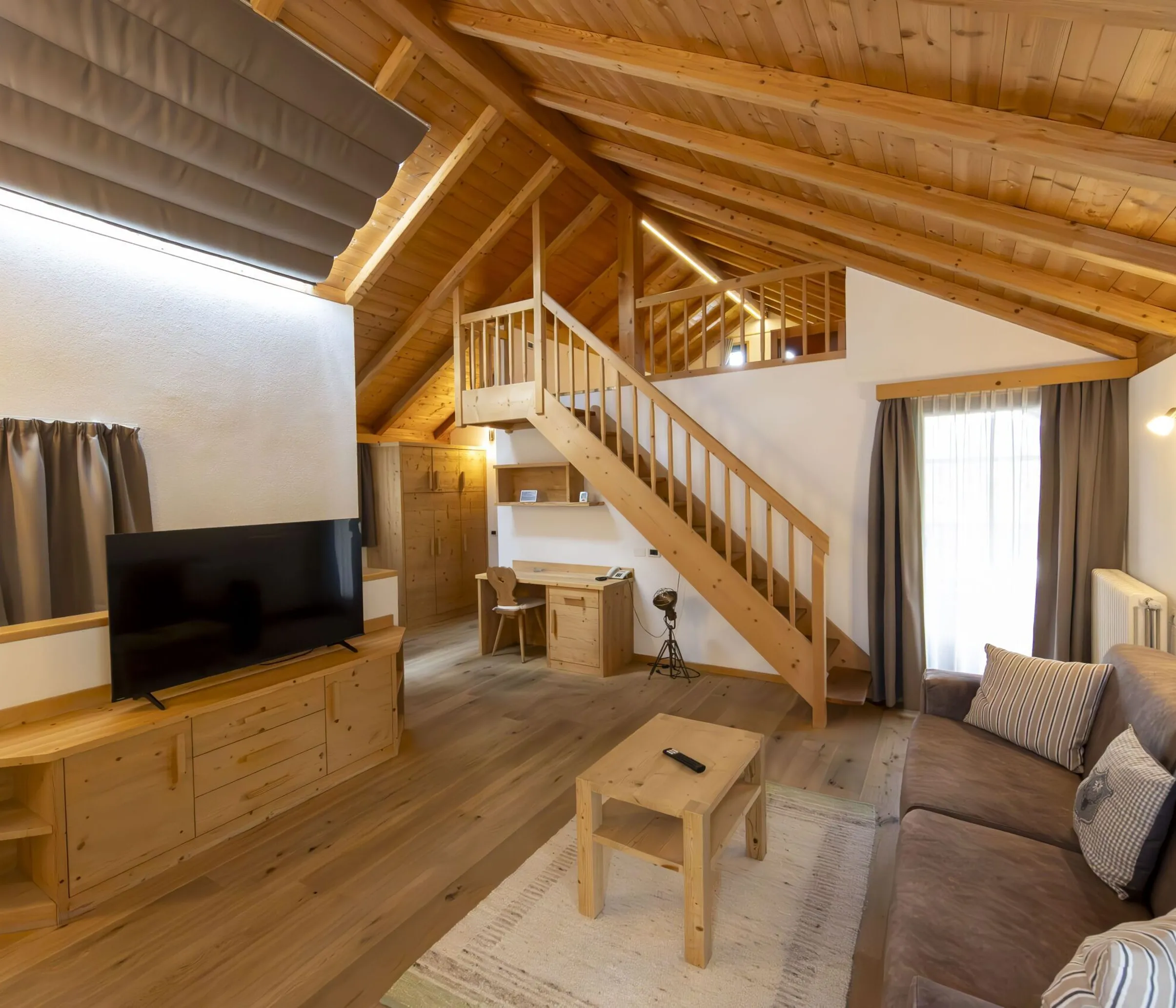 Cozy wooden living area with TV, sofa, coffee table, and a staircase to a loft in a cabin-style room