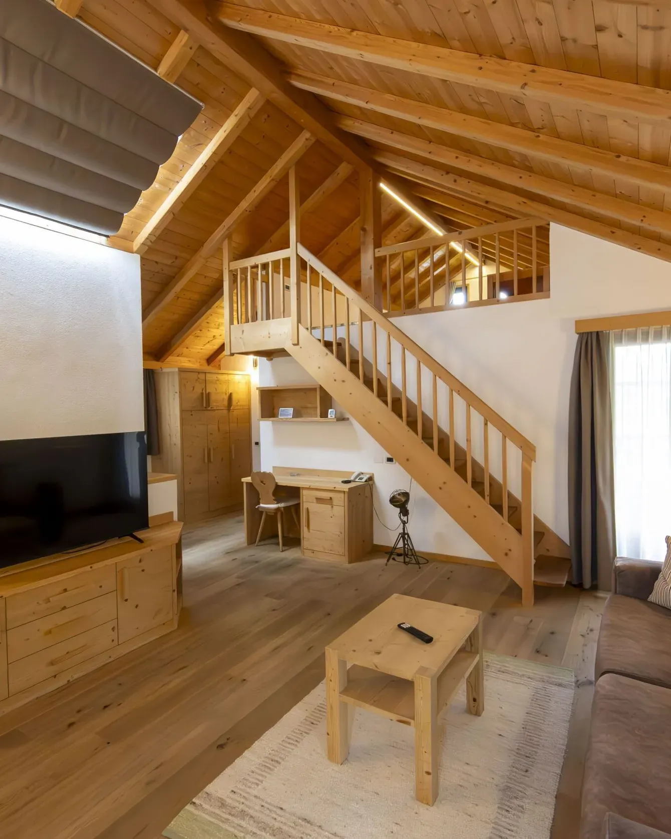 Cozy wooden living area with TV, sofa, coffee table, and a staircase to a loft in a cabin-style room