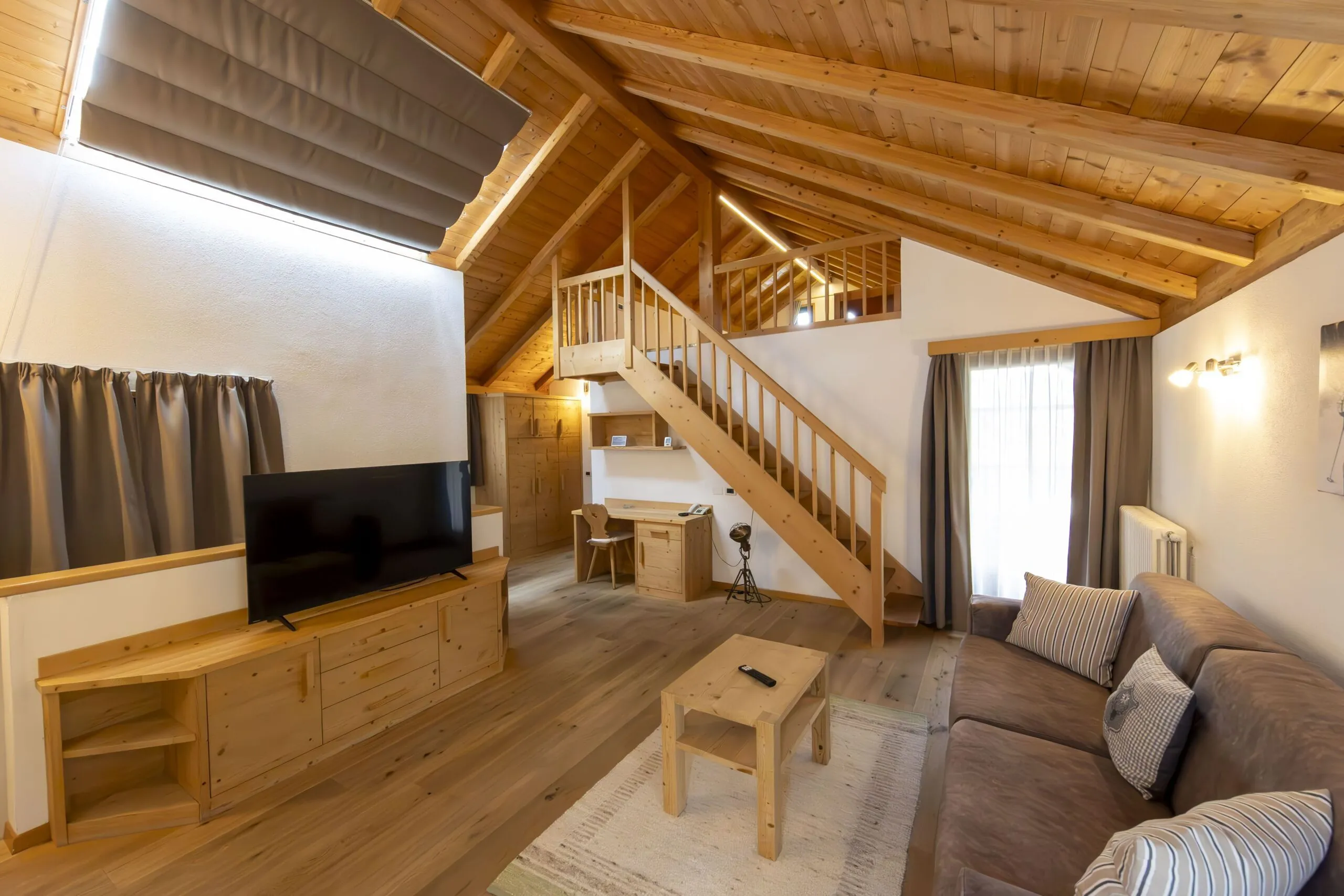 Cozy wooden living area with TV, sofa, coffee table, and a staircase to a loft in a cabin-style room