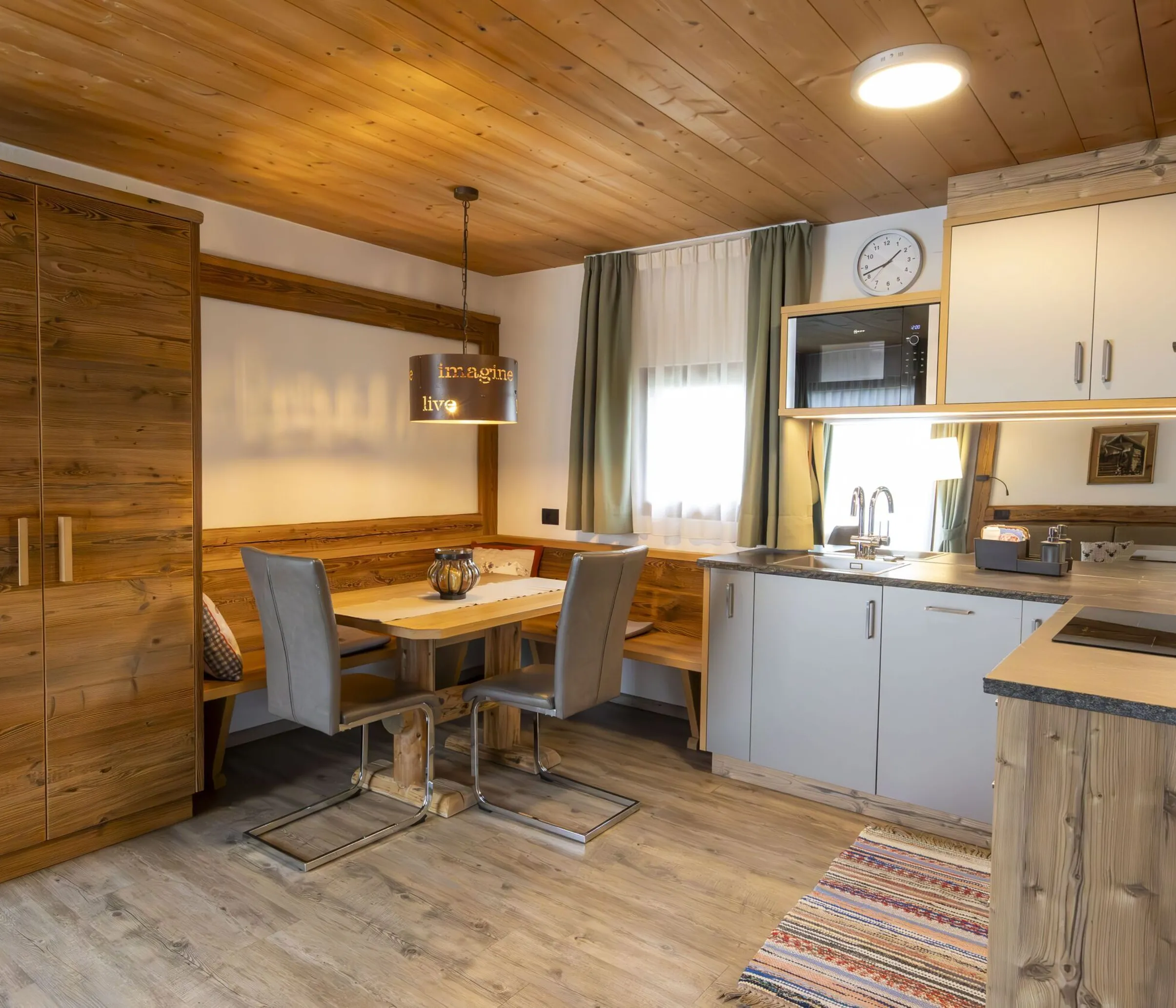 Cozy wood-toned kitchen and dining area with a bench, two gray chairs, and a hanging lamp.