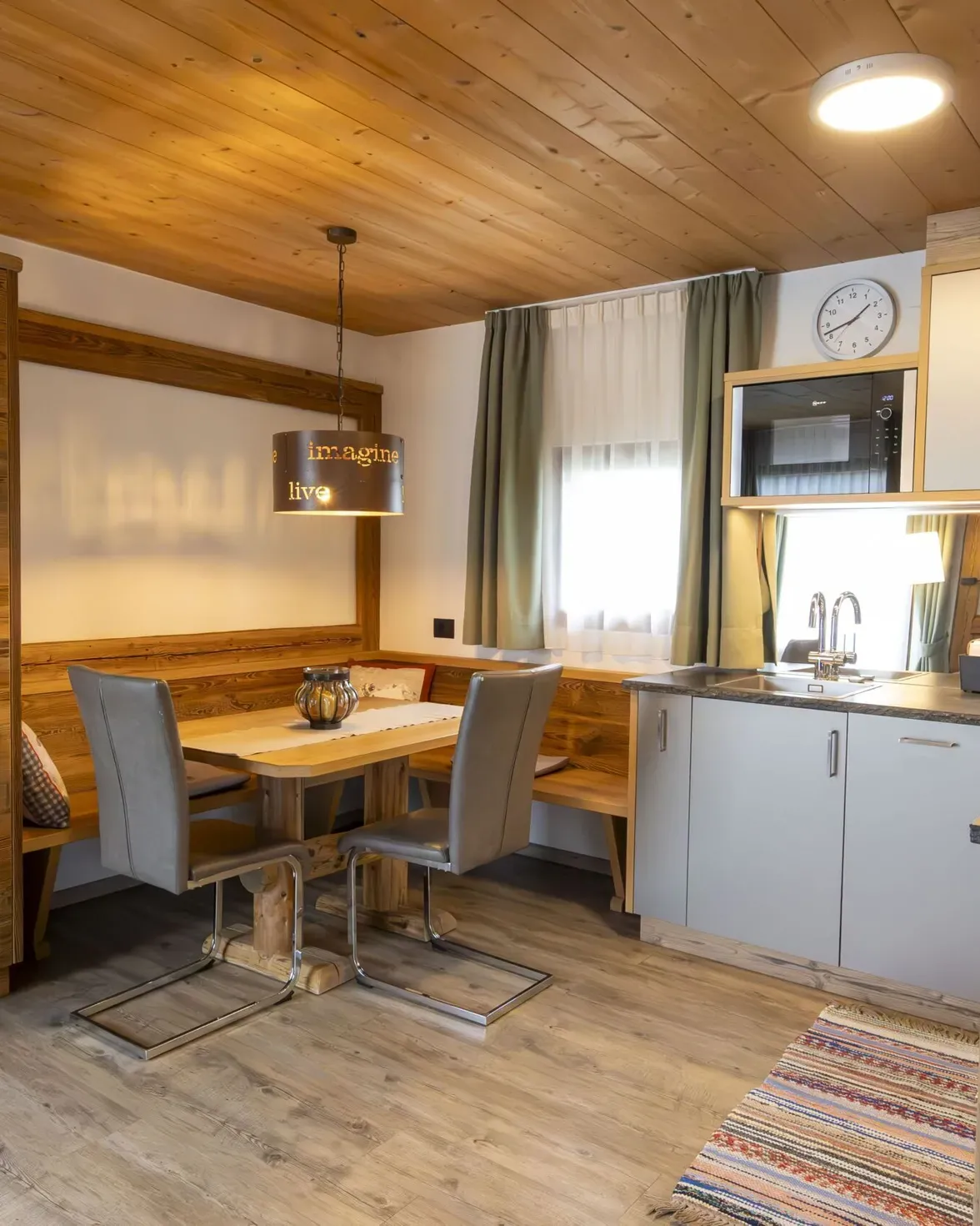 Cozy wood-toned kitchen and dining area with a bench, two gray chairs, and a hanging lamp.