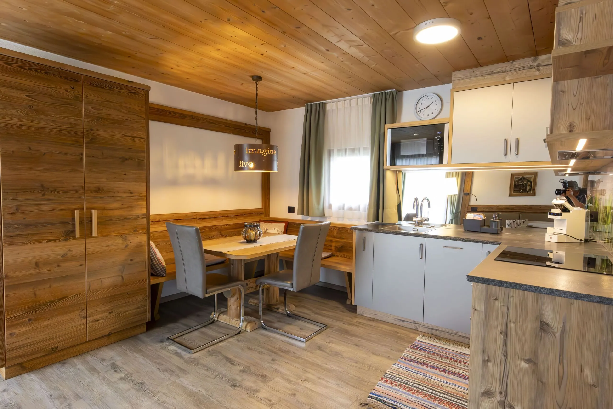 Cozy wood-toned kitchen and dining area with a bench, two gray chairs, and a hanging lamp.