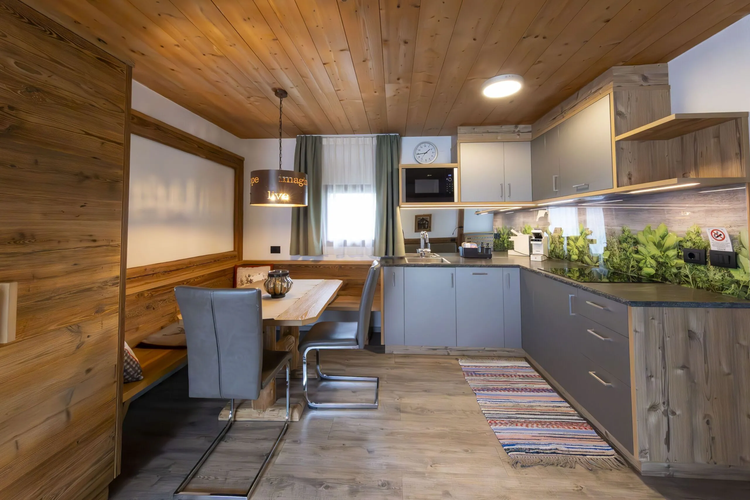 Cozy wood-paneled kitchen and dining area with gray cabinets, dining bench, and a green plant backsplash.