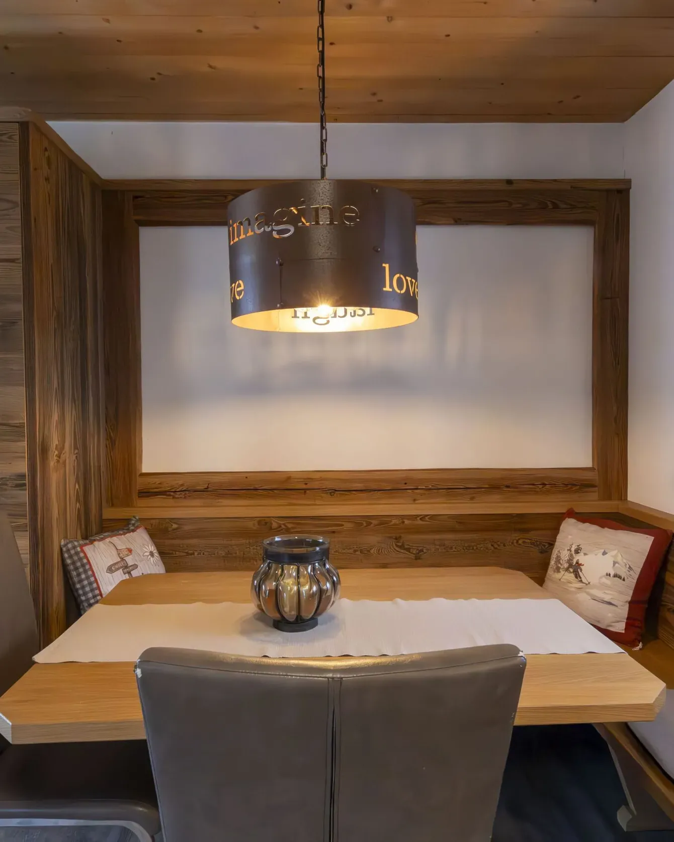 Cozy wooden dining nook with booth seating, frosted window panel, and a hanging lamp above the table.