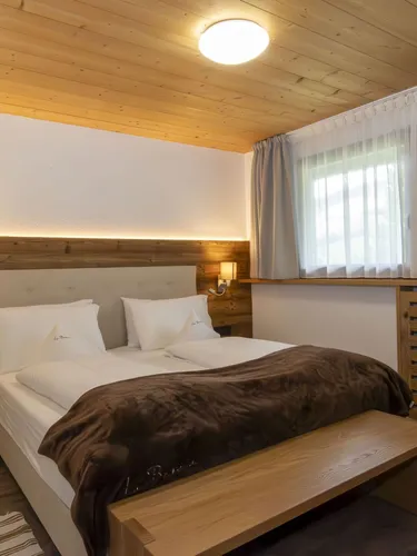 Cozy hotel bedroom with a wooden headboard, two white beds, brown blanket, nightstands, and large window with light curtains